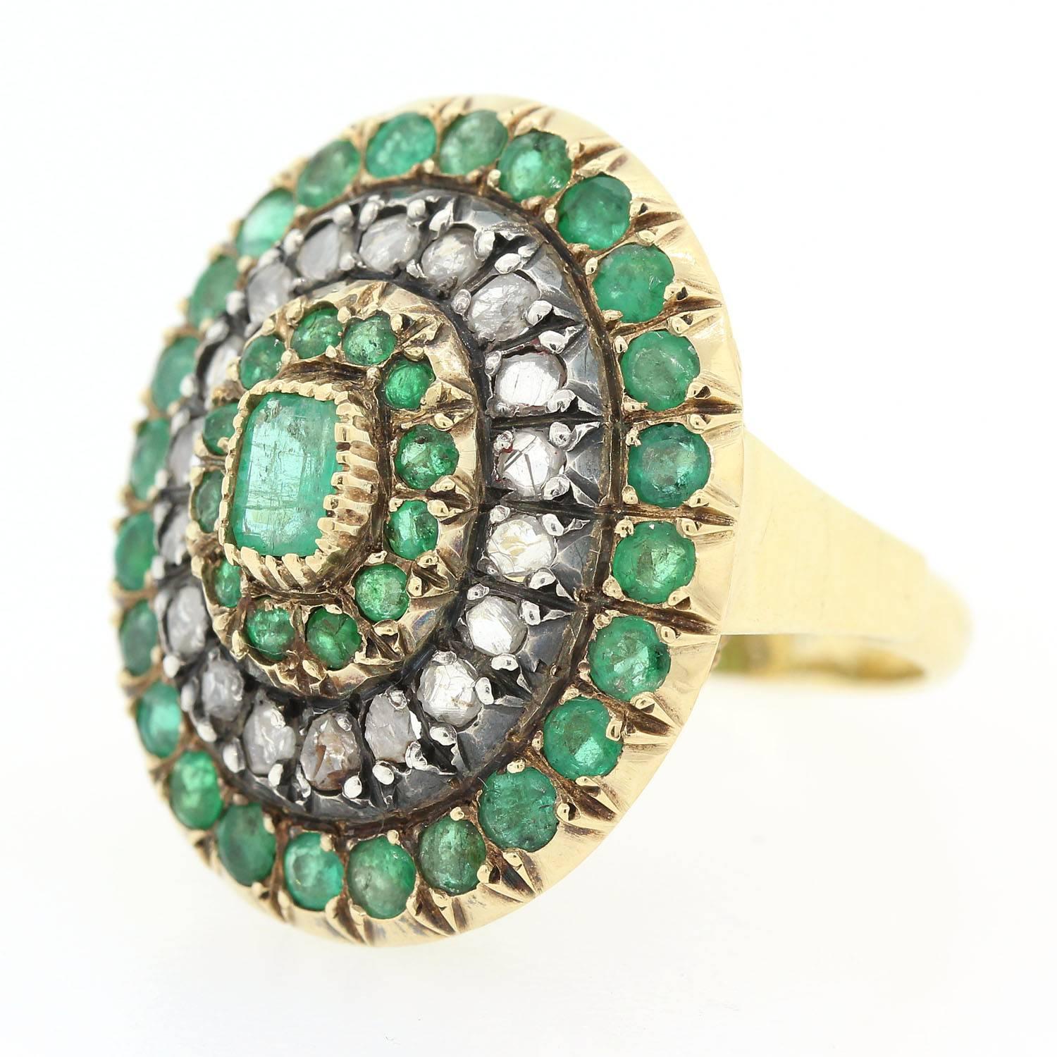 A playful oval shape 18KT gold and Silver ring, accented with a Rectangular Cut Colombian Emerald.  The Emerald is surrounded by twelve small Emeralds and two rows of  twenty Rose Cut Diamonds and twenty four Emeralds.  The setting is enhanced with