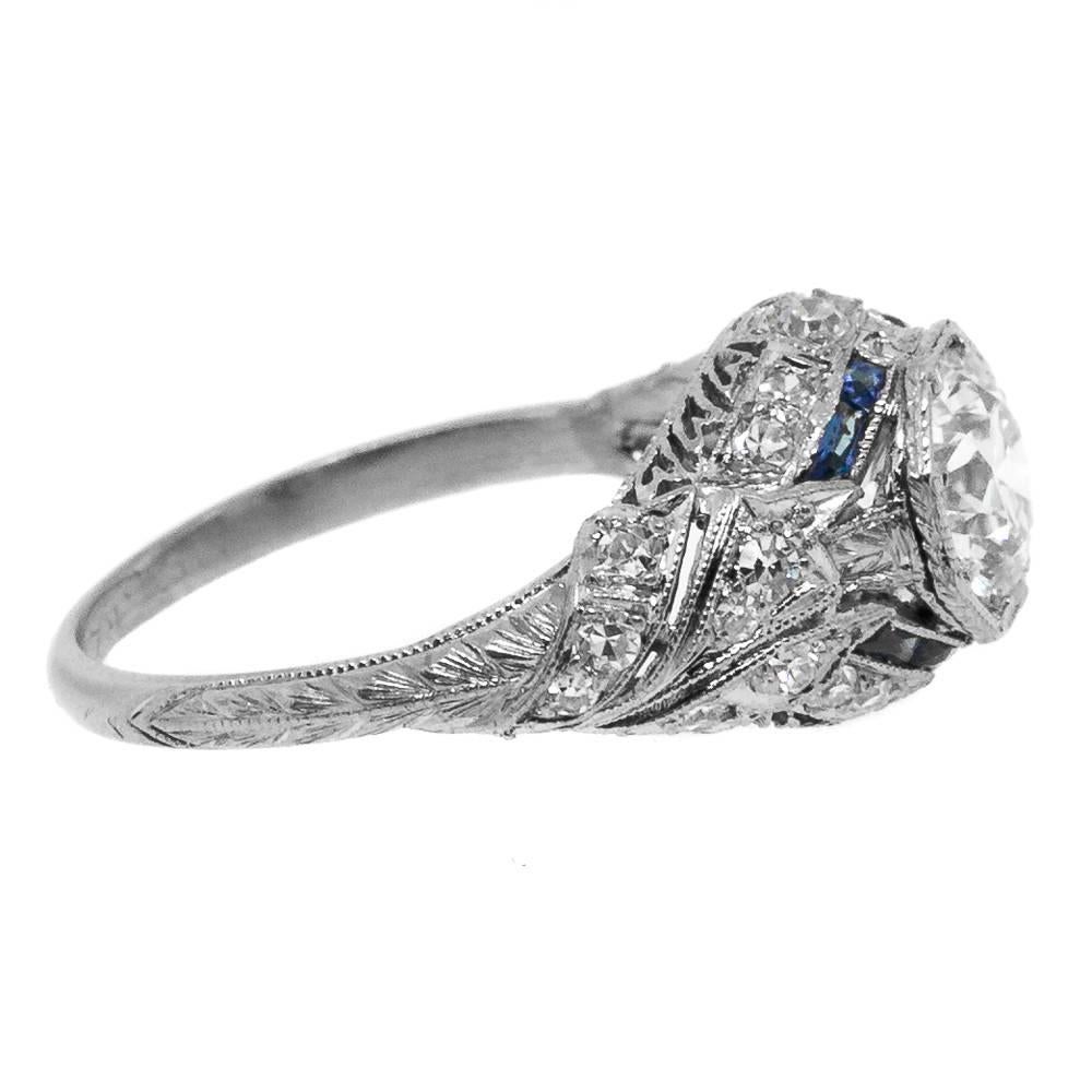 Beautifully coveted Art Deco platinum ring of delicate filigree work featuring an Old European Cut Diamond weighing 0.87 carat, certified J color - SI1 clarity.  
The ring is accented  with 8 calibrated  Baguette cut Ceylon Sapphires and 24 old