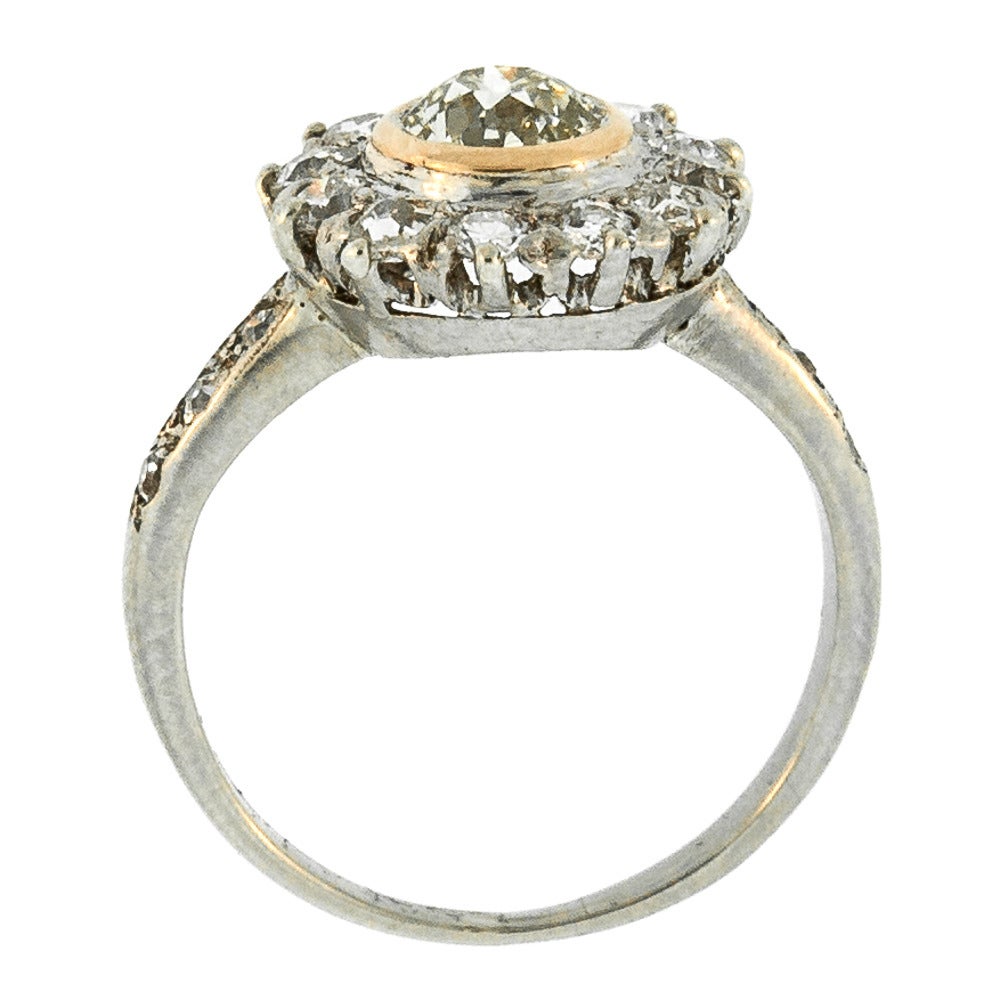 Antique Cluster Design Ring features an Old European Cut Diamond (VS2 clarity), placed delicately in a 14 KT Gold Bezel setting. Surrounded by Old Cut Diamonds, the hue of the Diamond evokes the dappled yellow light of dusk, reminiscent of a