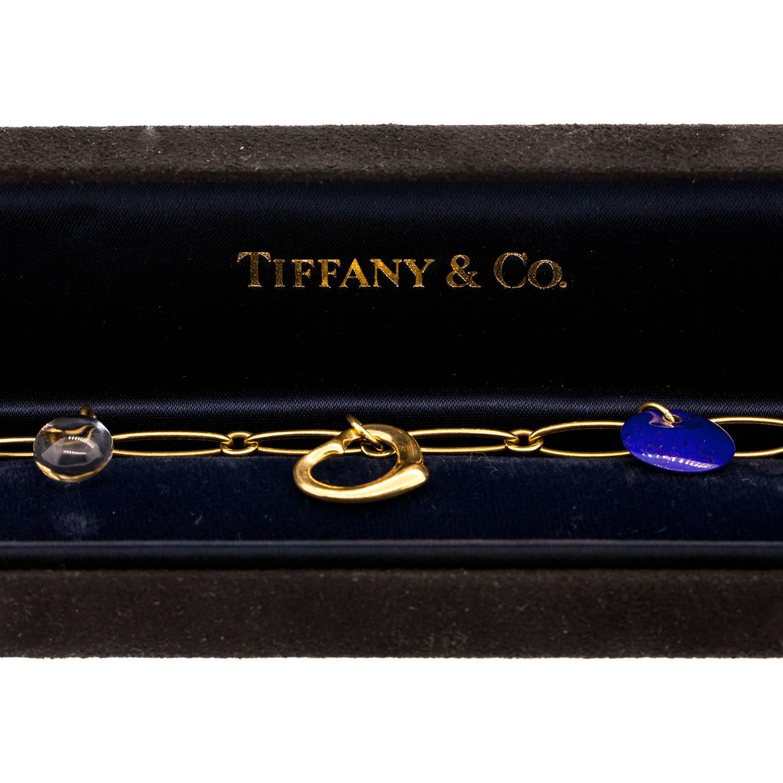 18KT yellow gold bracelet of open oval links and featuring 5 gem & gold charms., Lapiz Azul, Rock Crystal, red Jasper, Jade & gold open Hart.  The clasp is signed “Elsa Peretti – Spain Tiffany & Co.  750″.  Original box accompanies the