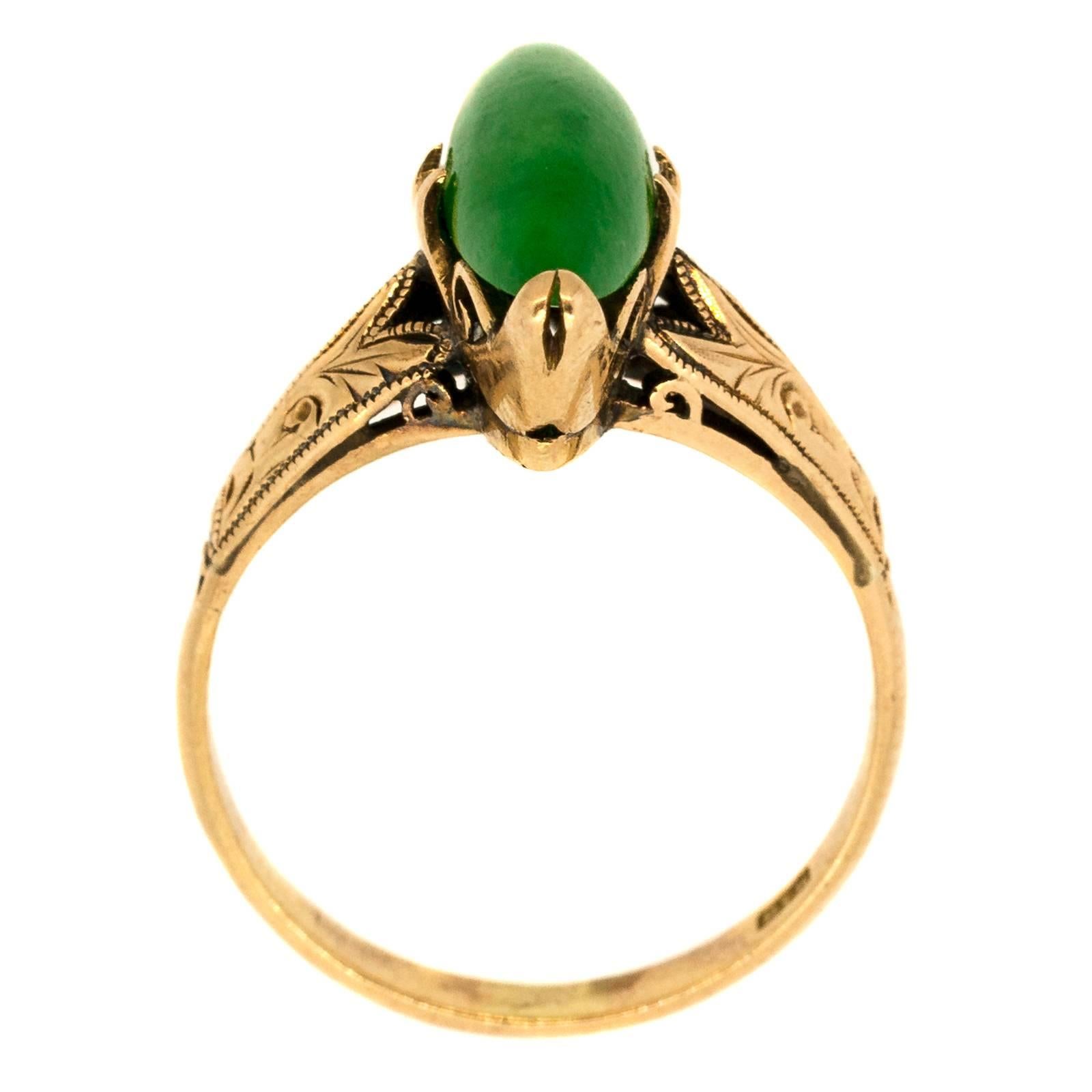 Circa 1920’s beautifully hand engraved 18KT yellow gold ring featuring a marquise cut cabochon natural translucent Jadeite.  The setting is enhanced with swirl prongs and hand engraved palm  design on the shoulders.  Delicate time worn milgrain