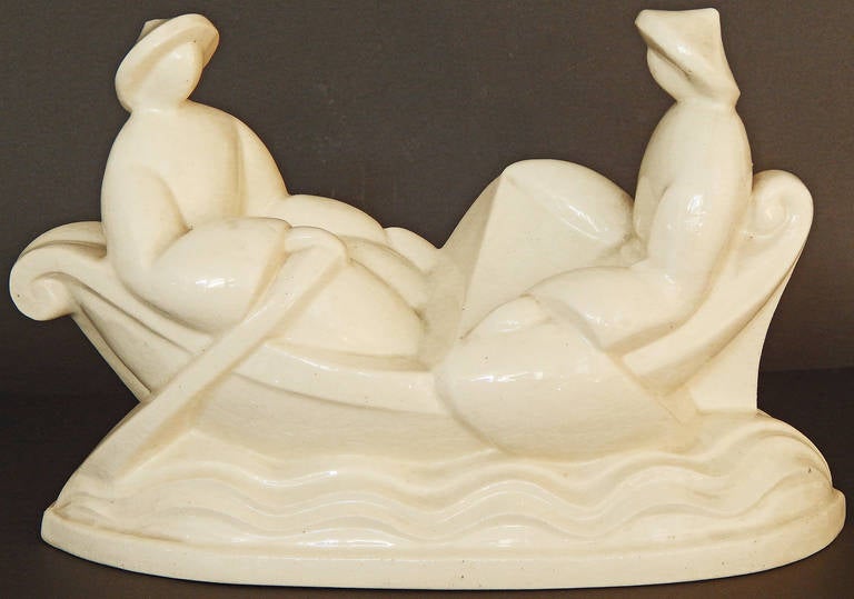 A classic example of Art Deco design heavily influenced by Cubism, this ceramic sculpture depicts two highly stylized Chinese figures in a curving rowboat upon an Art Deco sea, all enrobed in a creamy glaze with a subtle craquelure effect. This