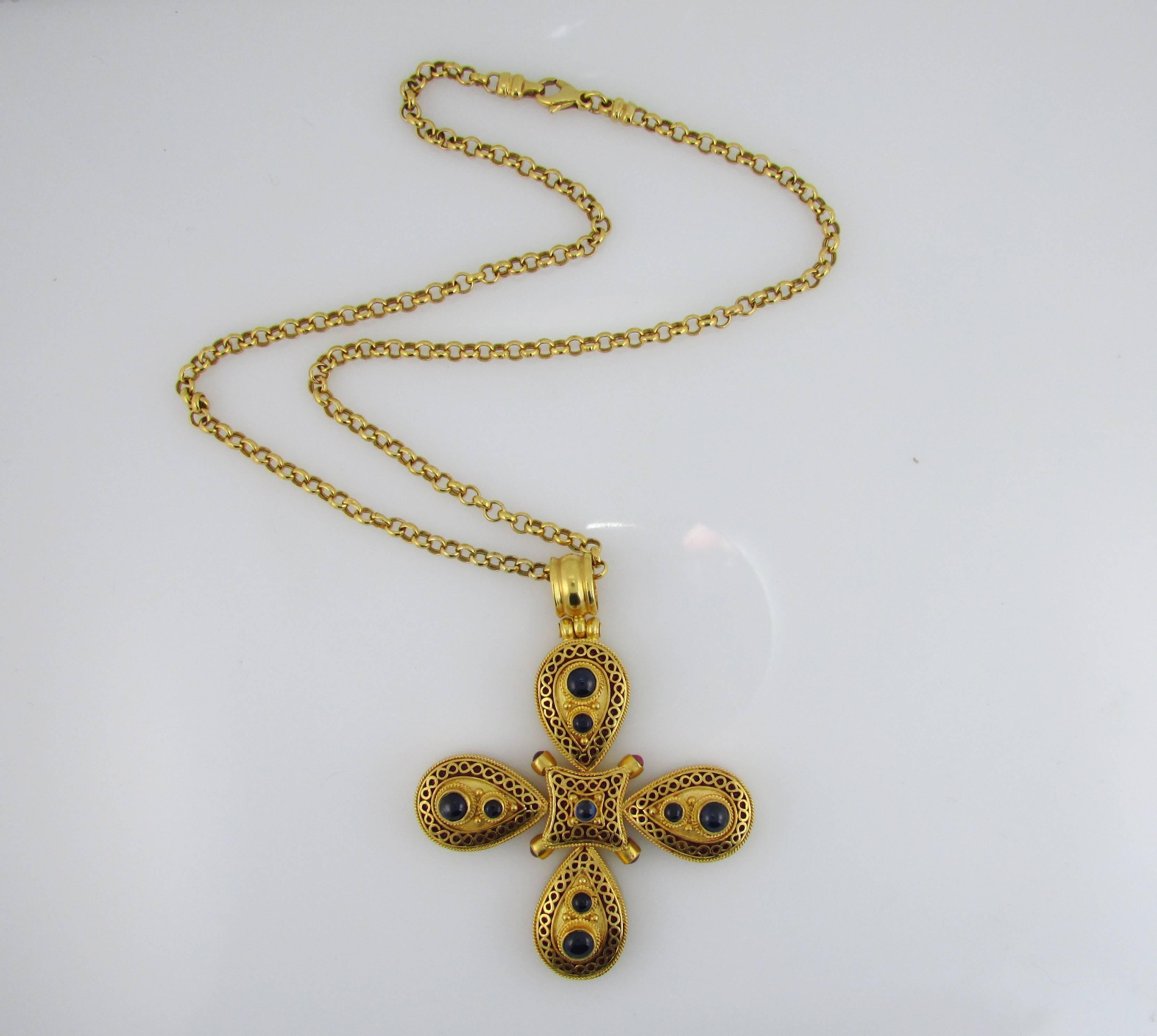 18KT yellow gold Maltese cross shaped pendant, set with 9 cabochon blue sapphires, 4 cabochon rubies, and decorated with red enamel. Comes with an 18KT yellow gold, 16.5 inch long round rolo chain. Signed Lalaounis. Cross is 2 inches square. 