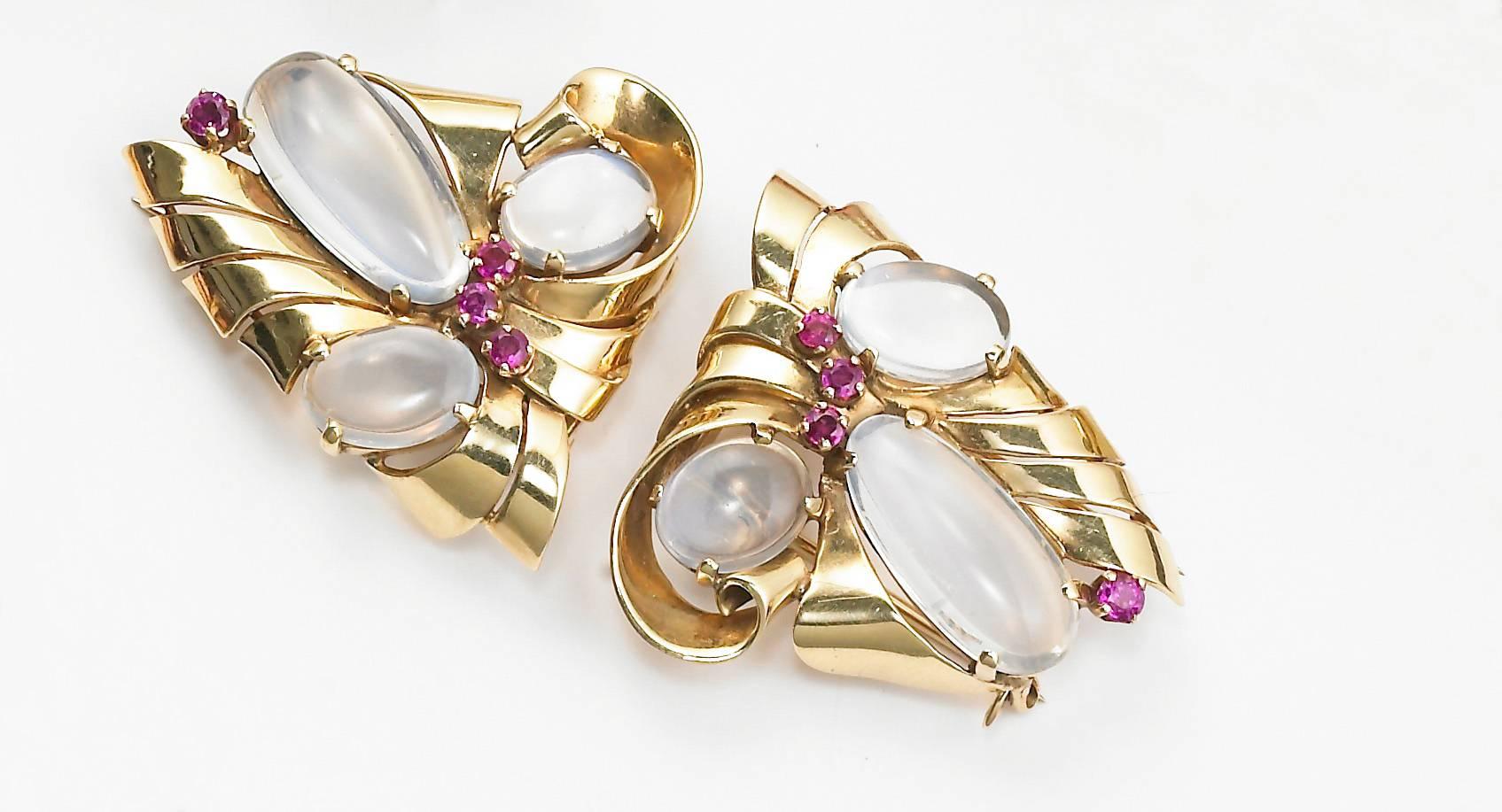 A beautiful pair of 14KT yellow gold clips with a scrolled design each set with three cabochon moonstones and accented with faceted round rubies. c1940s. Signed Raymond Yard.