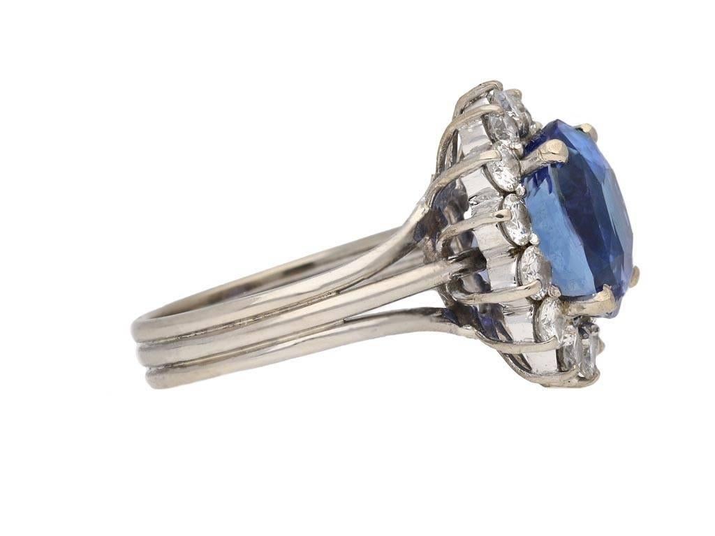 Vintage Ceylon sapphire and diamond cluster ring. Set to centre with a cushion shape old cut natural unenhanced Ceylon sapphire in an open back claw setting with an approximate weight of 8.14 carats, encircled by fourteen round brilliant cut