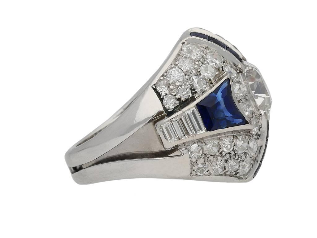 Art Deco sapphire and diamond ring. Set centrally with a round old cut diamond in an open back claw setting with a weight of 1.70 carats, additionally set with fourteen tapered step cut sapphires in open back rubover channel settings with an