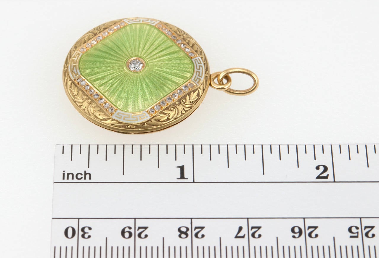 A unique locket featuring beautiful lime green and white guilloche enamel work and heavy foliate engraving in 18 karat yellow gold. A 0.05 carat diamond sparkles in the center of the locket alone with 32 additional tiny round diamonds that outline