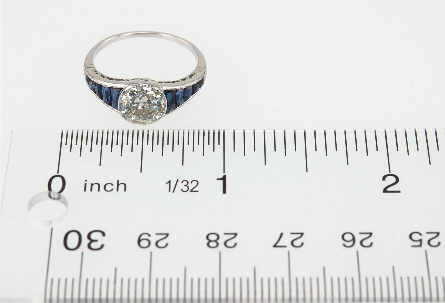 A gorgeous Edwardian diamond platinum engagement ring with 10 calibre cut blue sapphires.  The center bezel set diamond is an Old Mine Cut diamond that is approximately 1.65 carats and K in color and I1 in clarity.  This ring has a low profile and