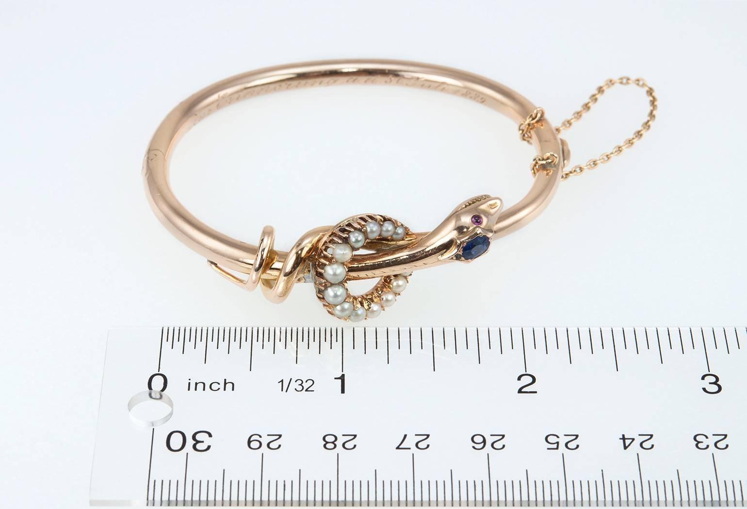 Victorian 14 karat rose gold snake bangle bracelet with a sapphire head and garnet cabochon eyes with 13 pearls set around the head.  The inside of the bracelet is engraved in script that reads 