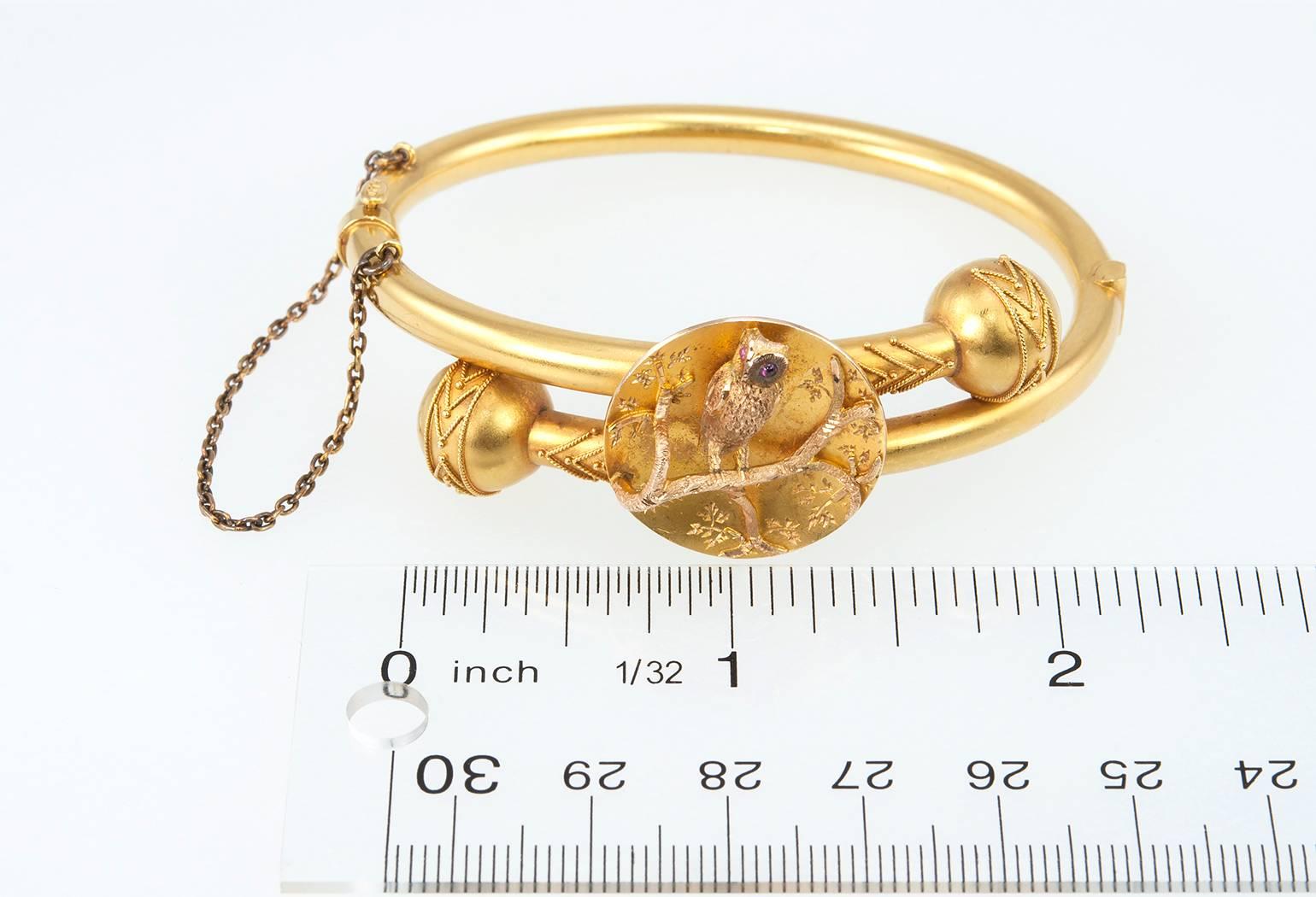 Victorian 14 karat yellow gold bangle bracelet in a beautiful matte gold finish.  The bracelet features an owl with 2 cabochon ruby eyes that is perched on a tree branch. Circa 1890s-1900s.
The bracelet measures approximately 6.5 inches in the