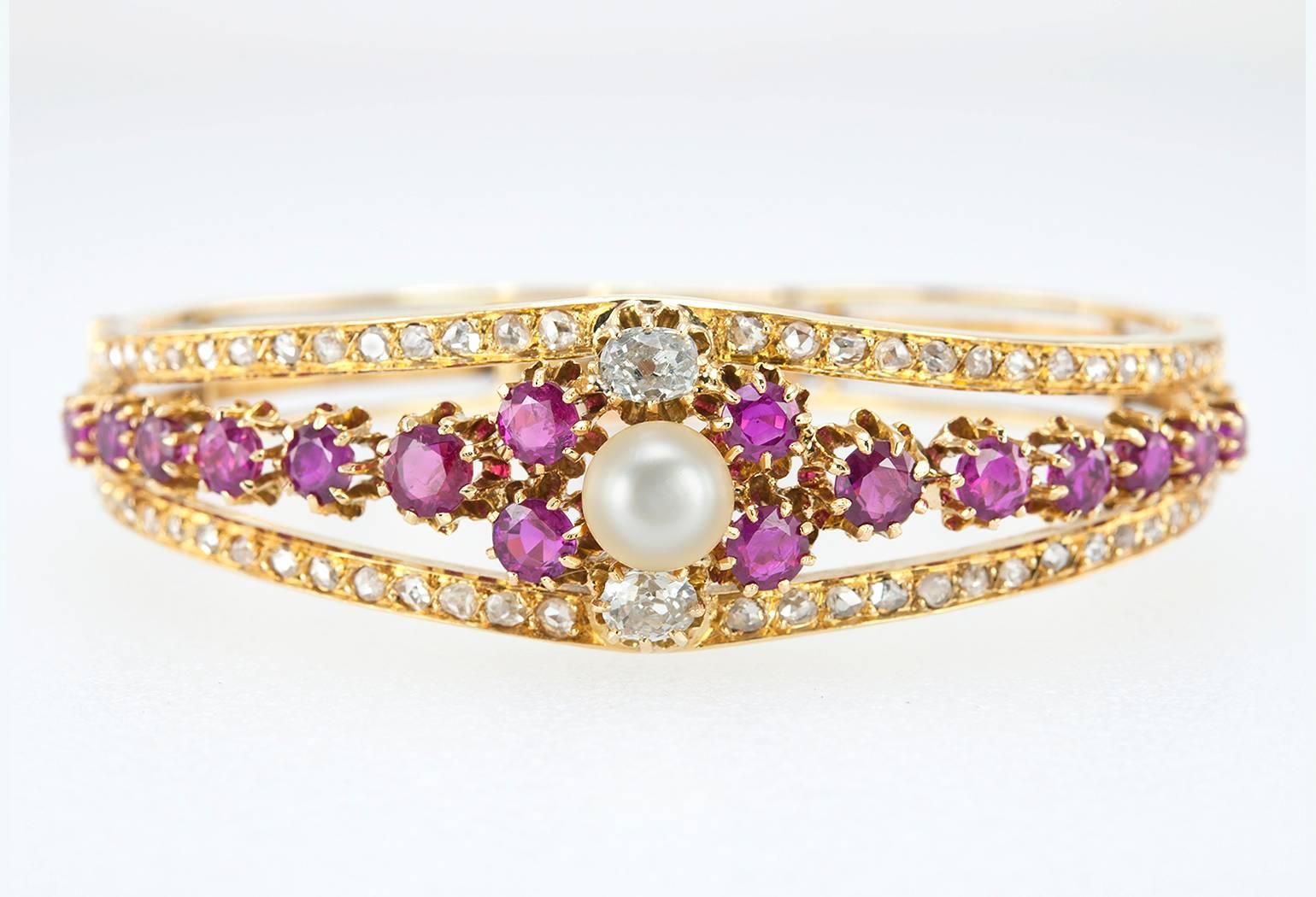 A Victorian 18 karat yellow gold bangle bracelet from circa 1880s-1890s.  This beautiful bracelet features 16 natural rubies that have an intense, gorgeous color along with a pearl set at the center and flanked by 2 old cushion cut diamonds. 