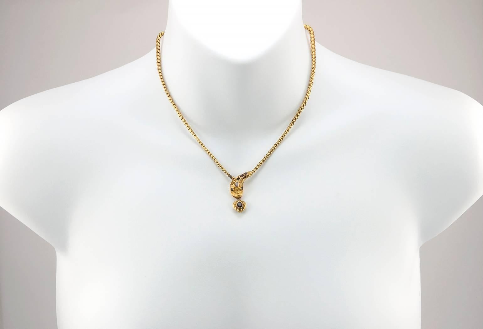 A Victorian gold snake necklace in 18 karat yellow gold.  This beautifully made necklace features a snake head with with 2 garnets for the eyes and 4 garnets along the head with a garnet heart charm coming out of its mouth.  The body of the snake