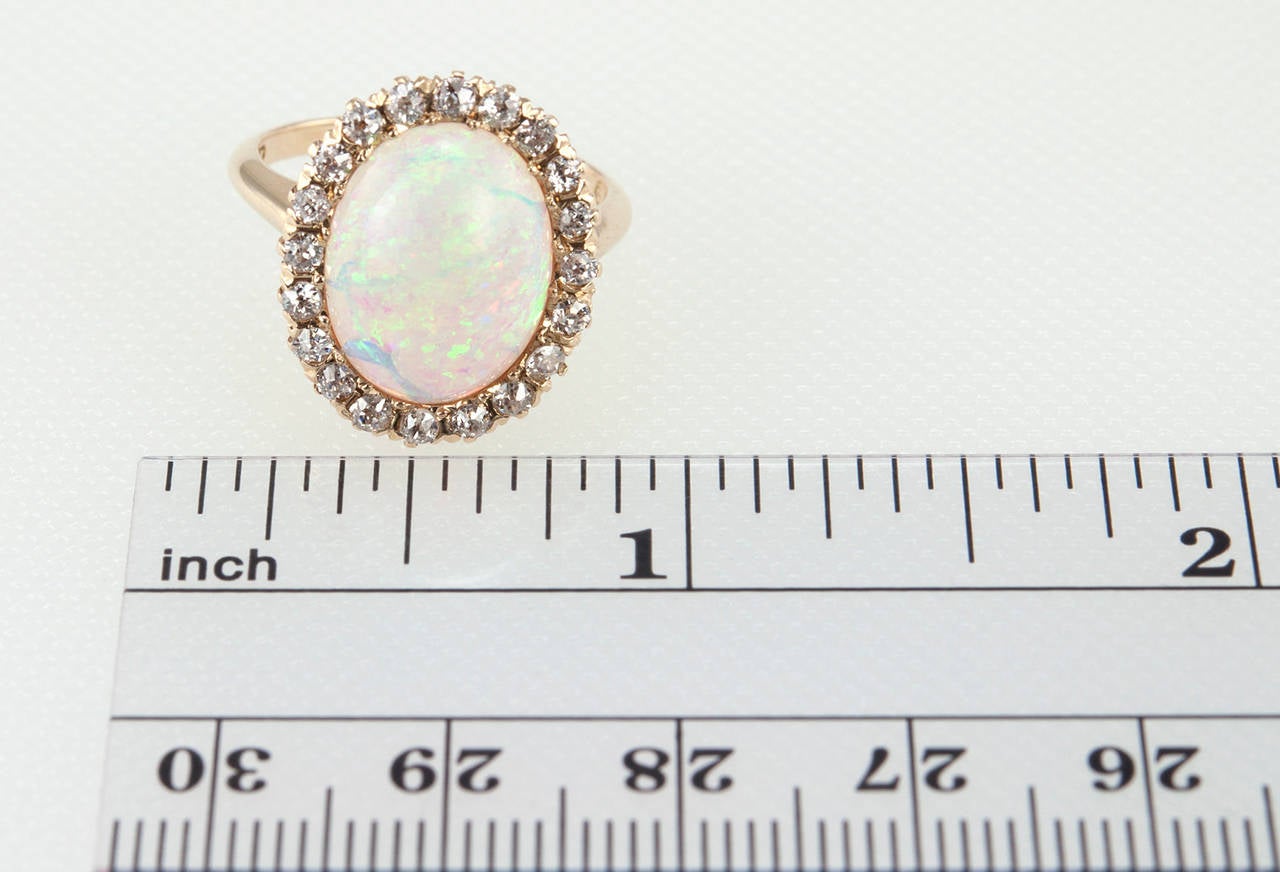 This beautiful Victorian opal cluster ring features a water opal, which shows great play of color, surrounded by 20 Old Mine Cut diamonds and 14 karat yellow gold. Circa 1900s. The ring does show indications of crazing that are appropriate with the