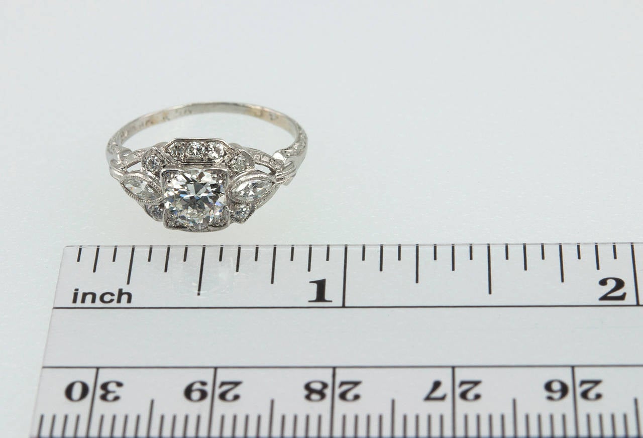 This Art Deco platinum engagement ring features a bright 0.58 carat G-VS1 (EGL) round brilliant cut diamond set in a square mounting with ten small round diamonds and two marquise shaped diamonds surrounding it. Circa 1930s. The setting is a low