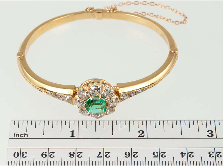Victorian bangle bracelet in 18 karat yellow gold, featuring a beautiful emerald and diamond cluster with graduated old mine cut diamonds on both sides. The emerald is approximately 2 carats and surrounded by 10 old mine cut diamonds, totaling