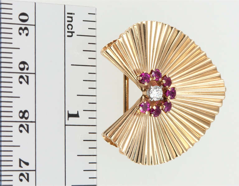 A perfect summer accessory! Tiffany & Co. fluted shell clip brooch in 18 karat yellow gold. 7 round brilliant cut rubies surround a .15ct round brilliant cut diamond. Circa 1960, signed Tiffany & Co. Approximately 1.24 inches long by 1.22 inches