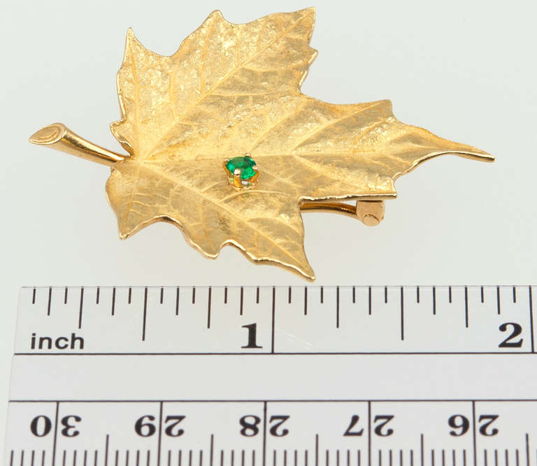 Tiffany & Co. leaf brooch in 18 karat gold chased to give the naturalistic texture of a maple leaf, set with a bright green emerald of 0.15ct in weight. Approximately 1.47 inches wide by 1.86 inches in length. Circa 1980 and signed Tiffany & Co 18KT.