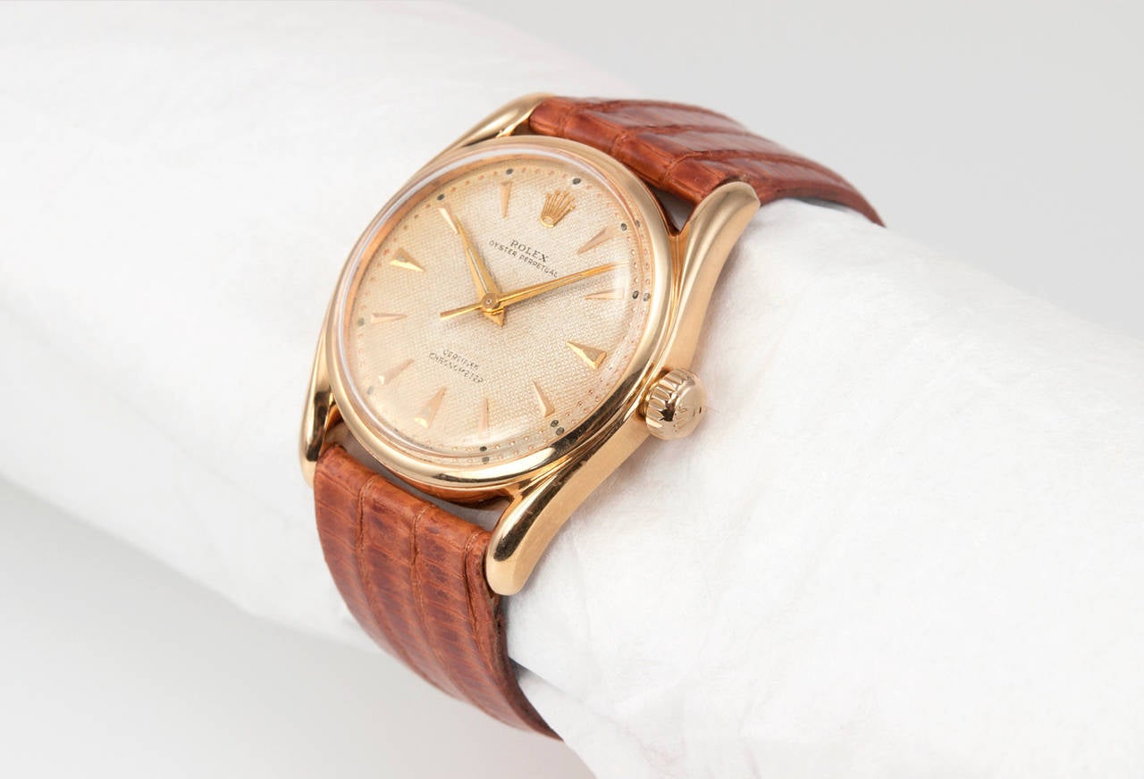 A rare Rolex watch with a Bombay style case, reference 6090. This 18 karat pink gold watch is from circa 1951 and features a waffle textured dial with pointed pink baton markers, a locking pink gold crown and plastic crystal. The case measures