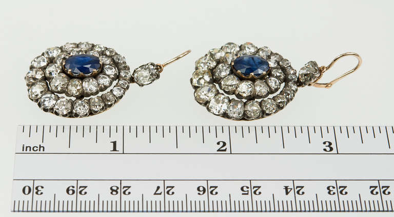 The ultimate cluster earrings! Victorian cluster dangle earrings with 2 concentric rows of old mine cut diamonds totaling 17 carats and a beautiful deep blue sapphire in the center totaling 4 carats. Set in silver and 18 karat gold, circa 1880s.