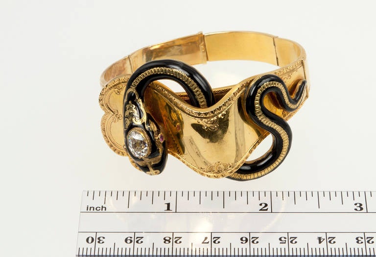 This unique Victorian hinged bangle bracelet in 18 karat yellow gold features a black enamel snake with approximately a 1.50ct Old Mine cut pear shaped diamond on it's head, circa 1870s; French hallmarks.

The widest part of the bangle is