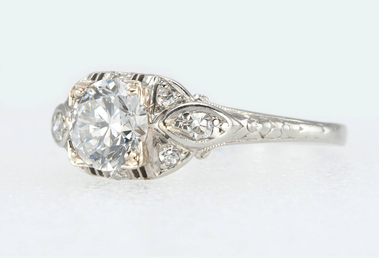 An Art Deco platinum engagement ring featuring a 0.96 carat round brilliant diamond that is F in color and SI1 in clarity (per EGL certificate) with nine small round diamonds set around the center diamond. It has a low profile so it is very