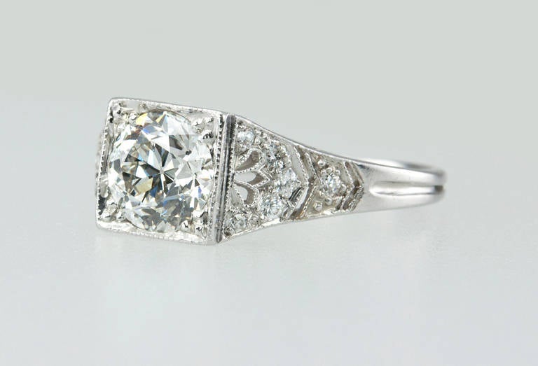 This lovely Art Deco platinum engagement ring features a bright and shiny Old European cut diamond center stone, 1.01ct G-VS2 (EGL) bead set in a square setting. The delicate filigree and small round diamond side stones add sparkle to this unique