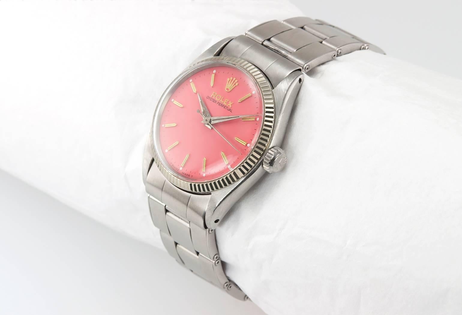 Rolex Oyster Perpetual stainless steel wristwatch, reference 6551. This MidSize Rolex watch features a plastic crystal, stainless steel waterproof crown, white gold fluted bezel, and a custom pink color dial on a classic Oyster riveted bracelet.