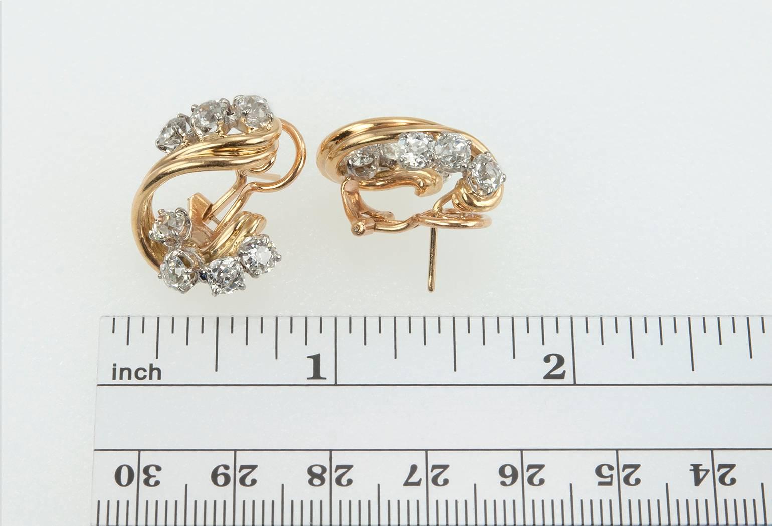 A beautiful pair of diamond 18 karat yellow gold and platinum twist drop earrings with omega backs that sit comfortably and securely on the ear.  These earrings features 14 Old European Cut diamonds that are each approximately 0.25 carats for a