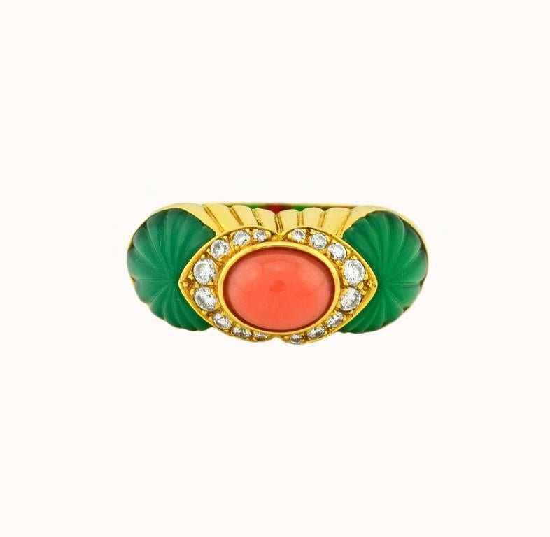 A striking Cartier 18 karat yellow gold ring featuring the beautiful combination of colors from the coral cabochon center and the carved chrysoprase side stones.  Additionally, 16 round brilliant cut diamonds are set around the coral, which total