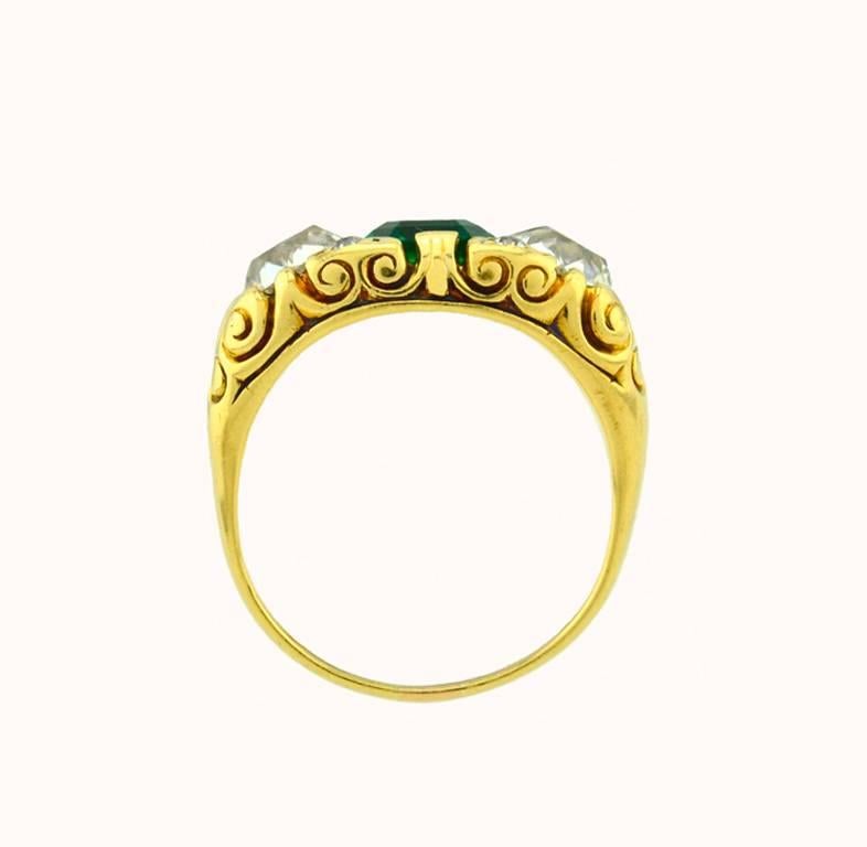 A stunning Victorian emerald and diamond three-stone ring in 18 karat yellow gold from circa 1900.  This gorgeous ring features a 1.21 carat natural Columbian emerald (natural, oiled Columbian emerald per AGL certificate) in the center flanked by 2