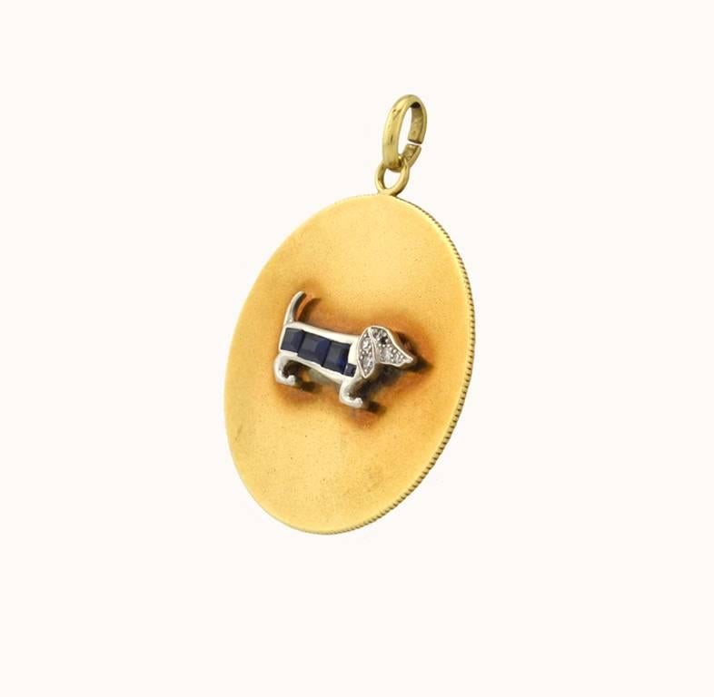 A fantastic vintage 1950s large-scale dog charm in 14 karat yellow gold and platinum.  This charm features a dachshund dog in diamonds and sapphires on a gold disc. The dog measures approximately 0.86 inches in length.

This charm measures