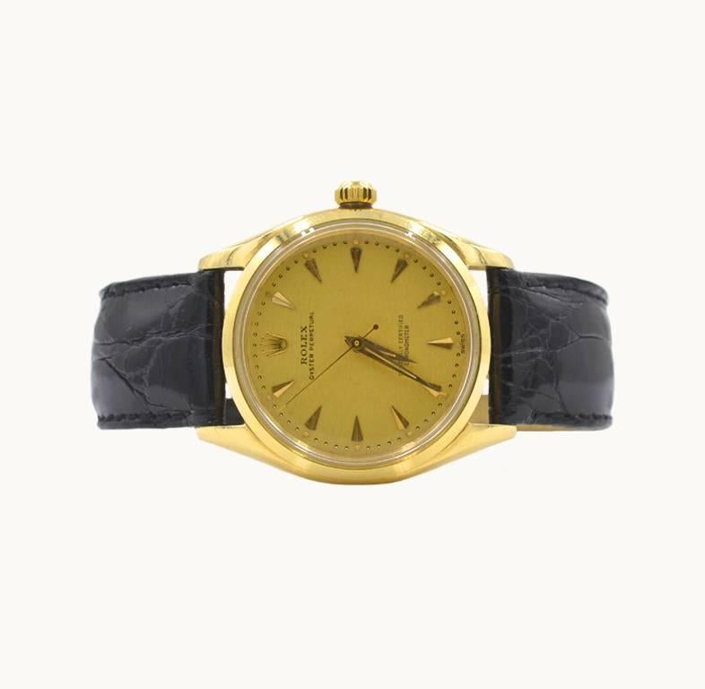 This vintage Rolex oyster perpetual wristwatch in 14 karat yellow gold, reference 6567. This beautiful Rolex features an original champagne color linen dial, locking yellow gold crown, plastic crystal, 14 karat yellow gold case, oyster perpetual