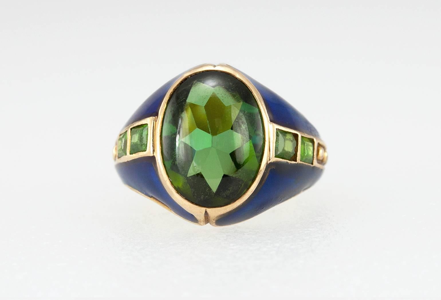 This incredible Arts and Crafts 18 karat yellow gold ring was made by Tiffany & Co. around the turn of the century. It features a bezel set peridot cabochon with two demantoid garnets on each side with beautiful blue enamel. Circa 1900s.  A truly