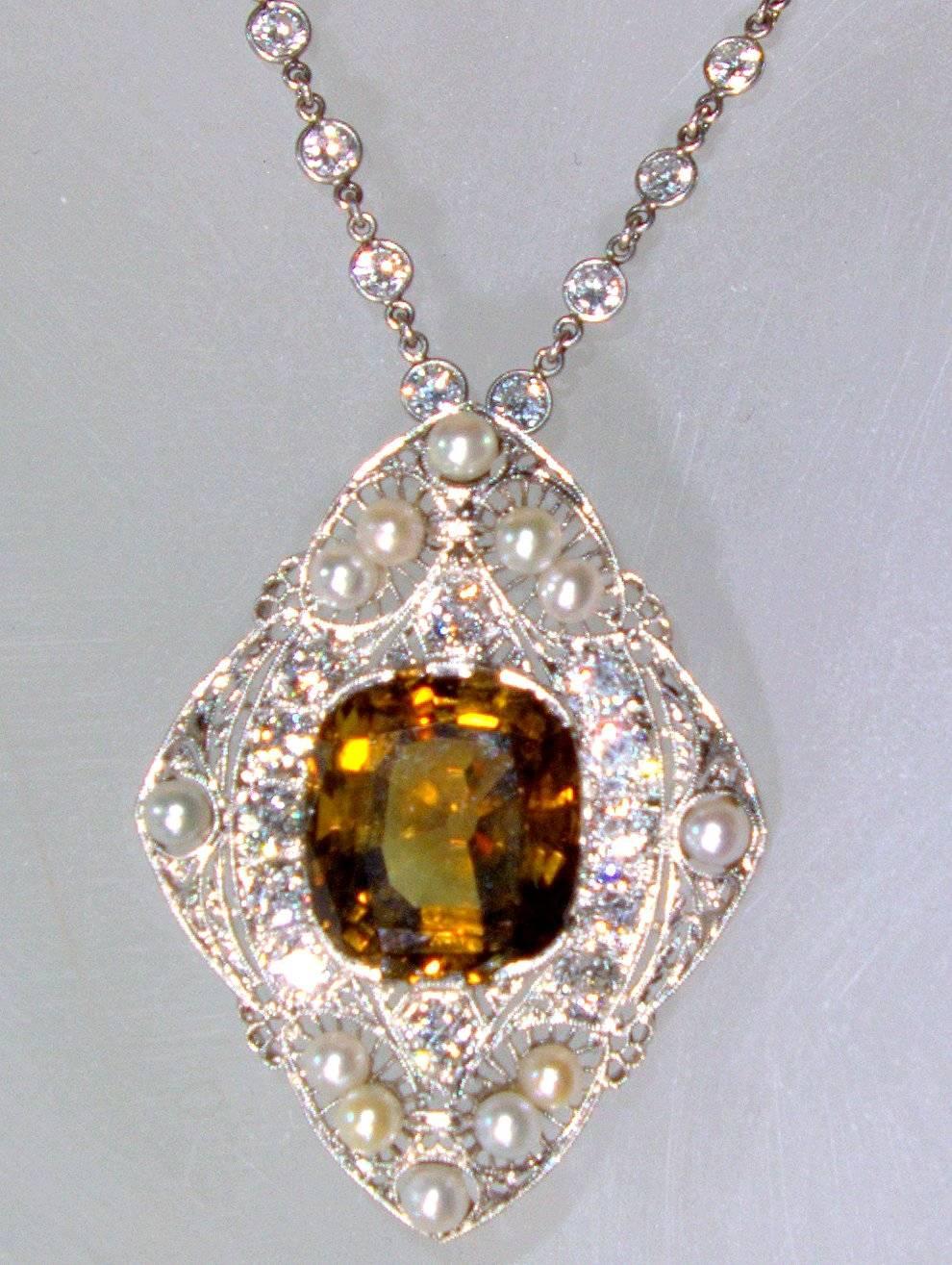 Circa 1915 and probably American this pendant suspends from a modern diamond chain that possesses 5 cts.  The unusual center stone is a mine cut chrysoberyl weighing approximately 14 cts.  It is a bright golden root-beer color.  There are 12 round