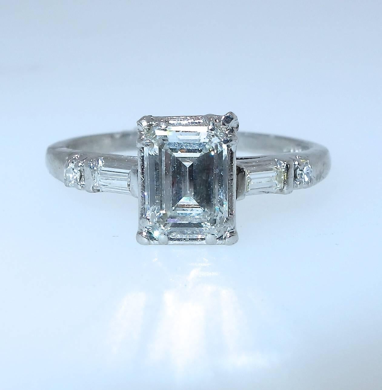 The handmade platinum mounting centers an emerald cut diamond.  Color H/I, and clarity VS2.  This well cut stone weighs 1.0 cts., and is accented with a round and baguette cut diamond on either side.  The total diamond weight is approximately 1.15