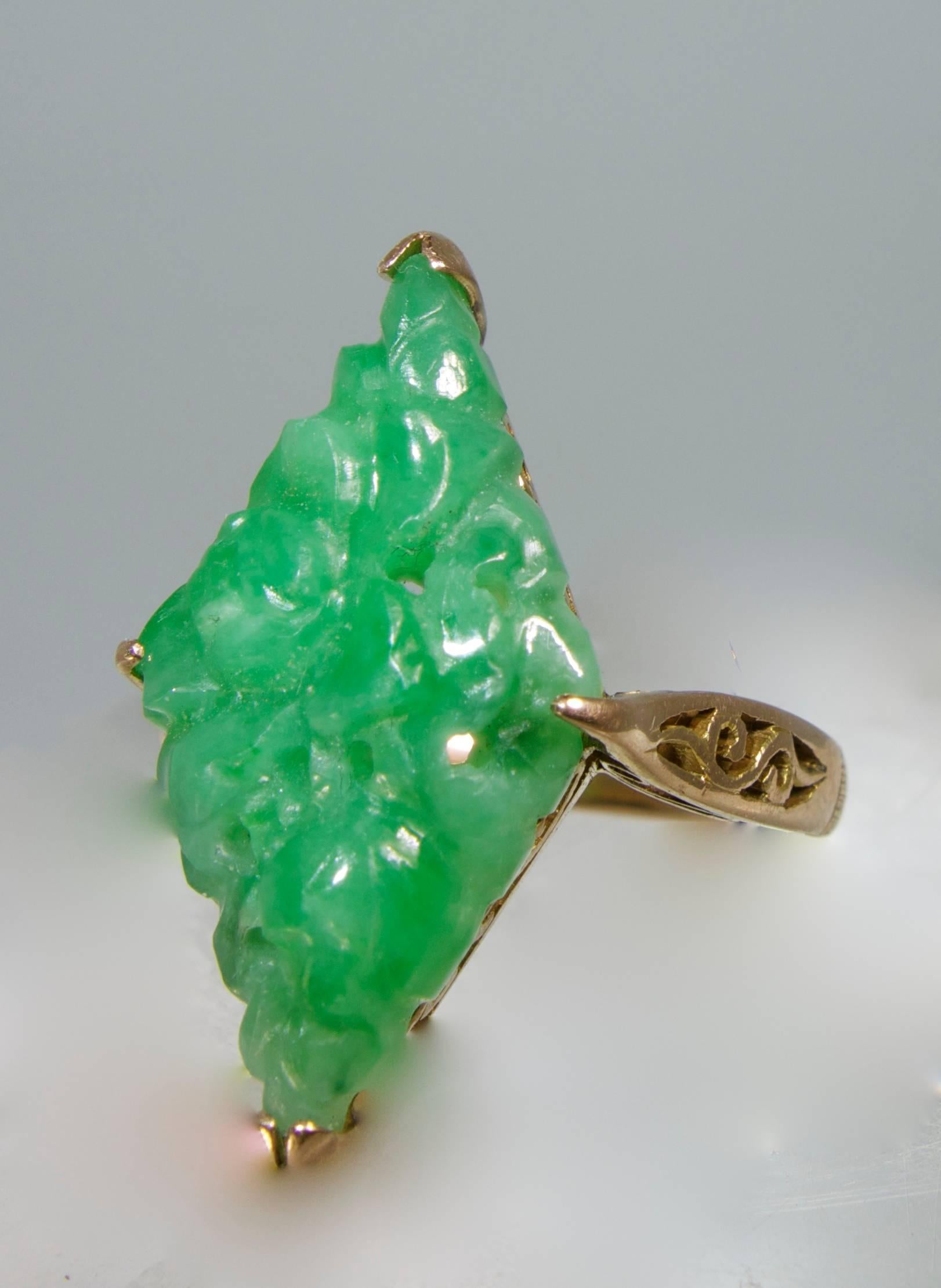 The rose (or pink) gold ring with delicate cut out work centers a carved (in a delicate floral motif) medium to medium light green color natural jadeite jade. The jade measures 21 mm by 12 mm by 4.5 mm (deep).  The ring tests 14K, there are (non