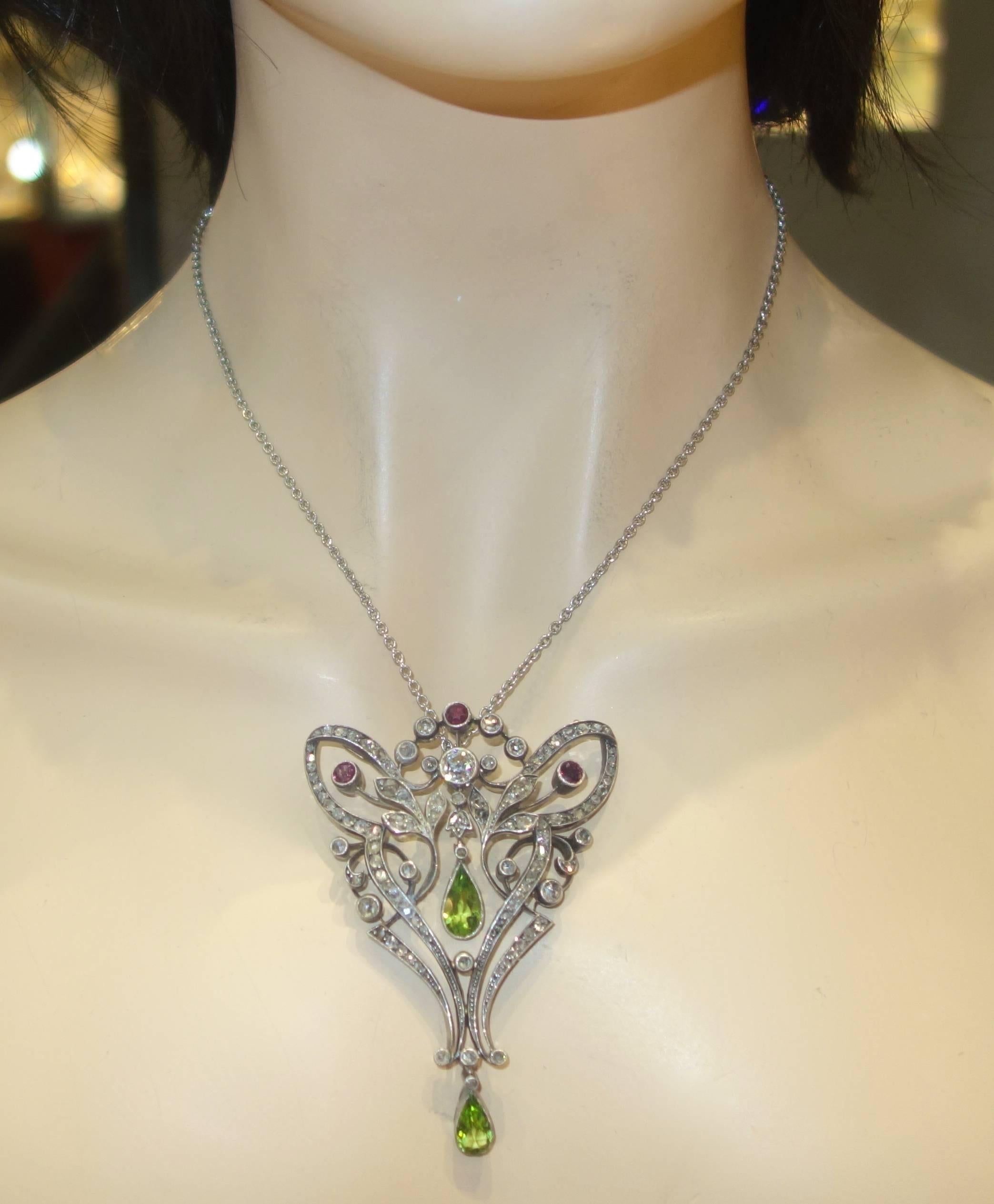 Rose cut and old mine cut diamonds are set with rubies (approximately 1 ct.) and centers two fine peridots in this silver topped gold long pendant which has an attachment so that it can be worn also as a brooch.  The fine green pear cut peridot