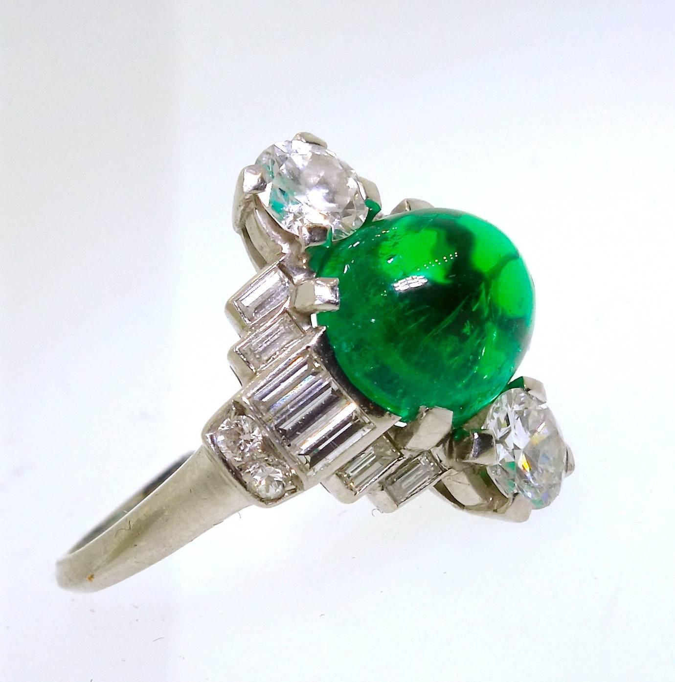 The center Colombian emerald displays a fine deep green color.  This high cabochon cut stone weighs approximately 3.5 cts.  The color is remarkable reminding one of a small green "jelly bean".  Fine baguette cut diamonds and round diamonds