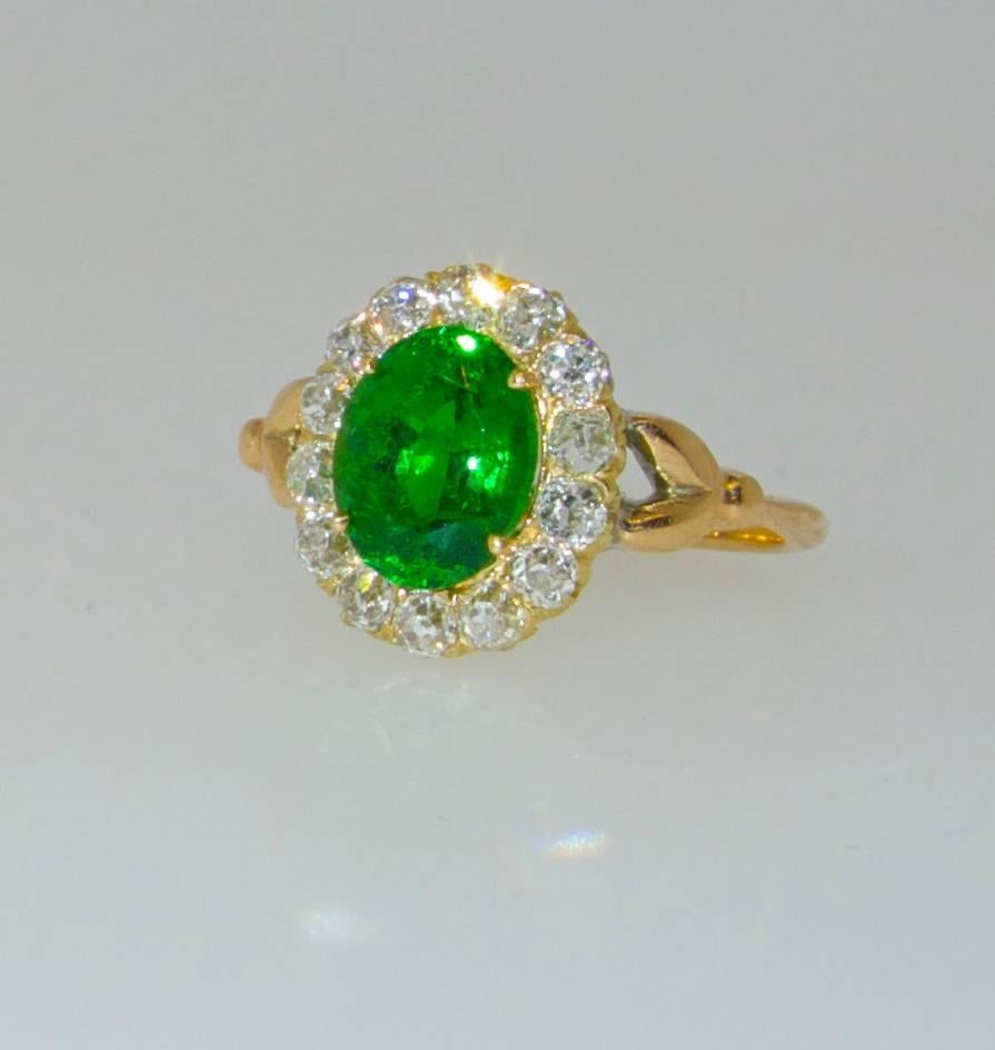 The fine quality Tsavorite (green garnet) weighs just over 1 ct. The color is a bright vivid green.   It is accompanied by a AGL certification.  It is surrounded by 14 old cut diamonds weighing approximately .50 cts.  This antique ring can easily be