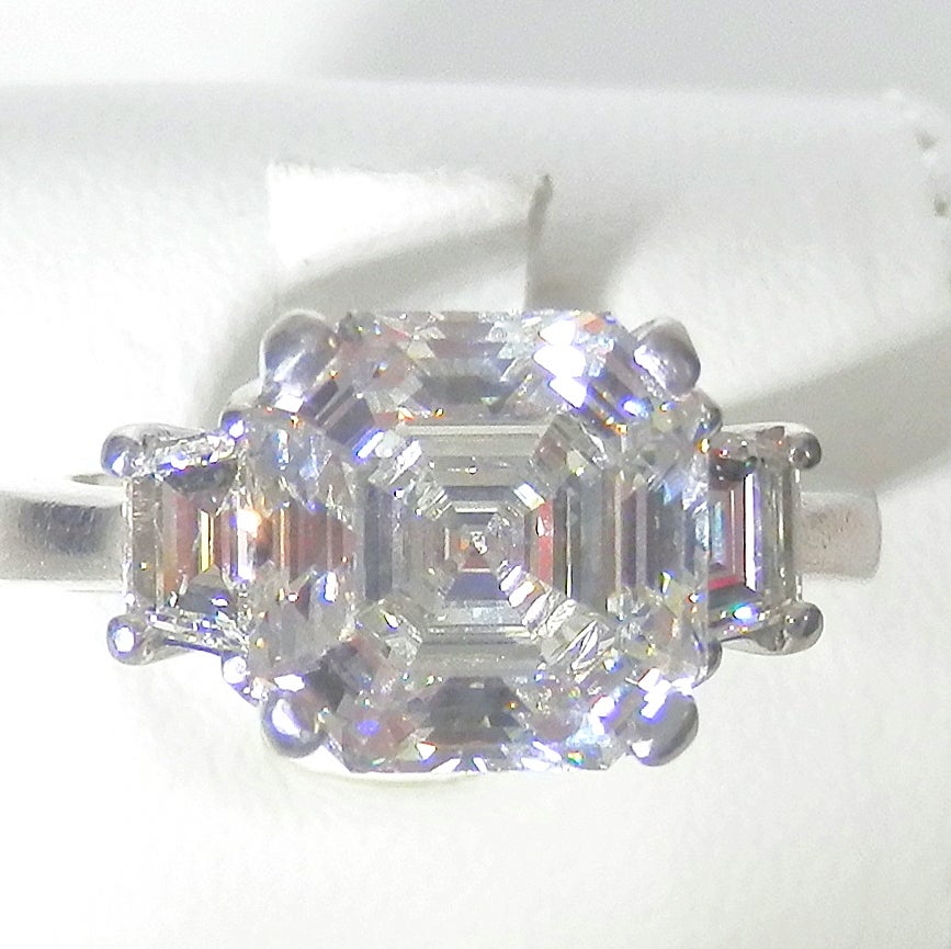 The center diamond is a Royal Asscher Cut diamond weighing 4.19 cts. It is accompanied by a recent GIA certificate stating that this diamond is J,VS1.  It has medium blue fluorescence (which is a plus for this stone as it will make the diamond