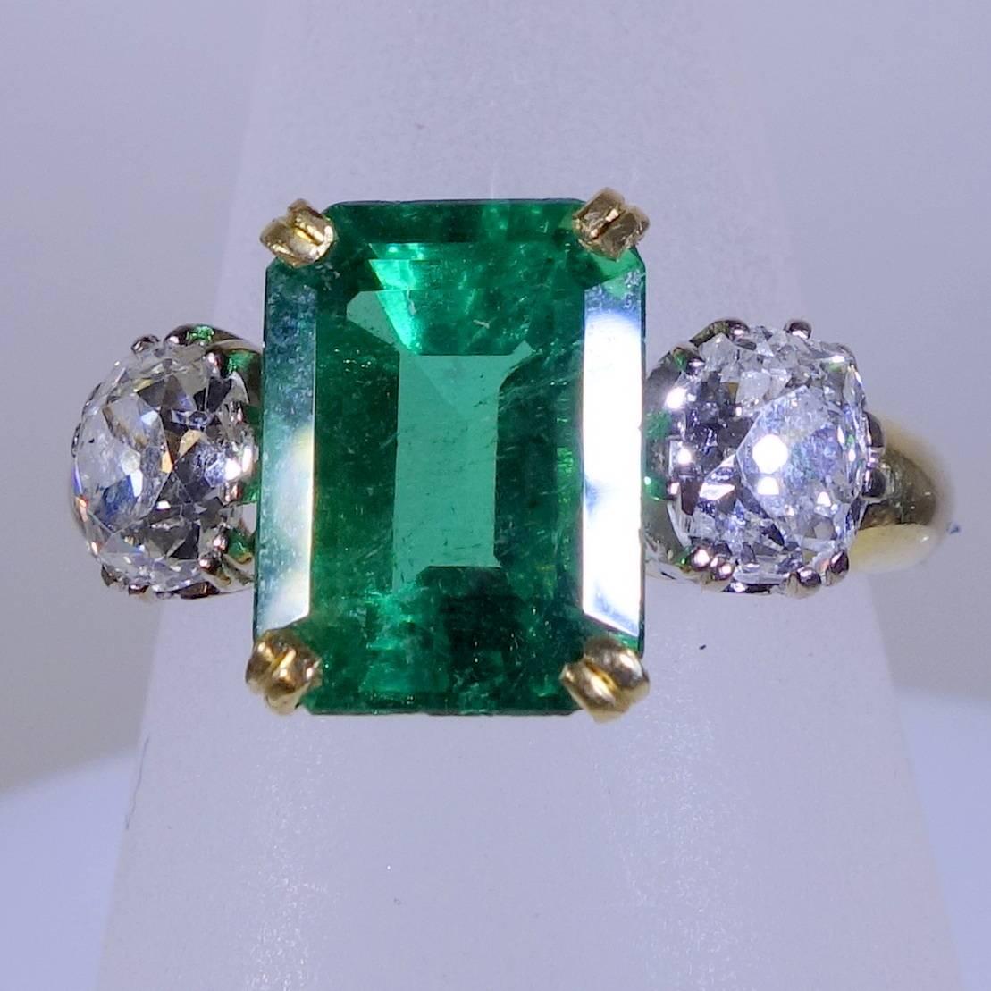 18K yellow gold  ring possessing a center 4.48 ct. Colombian emerald.  There are approximately 1.60 cts. of European cut diamonds on either side of this bright green stone.  Circa 1900.  English.