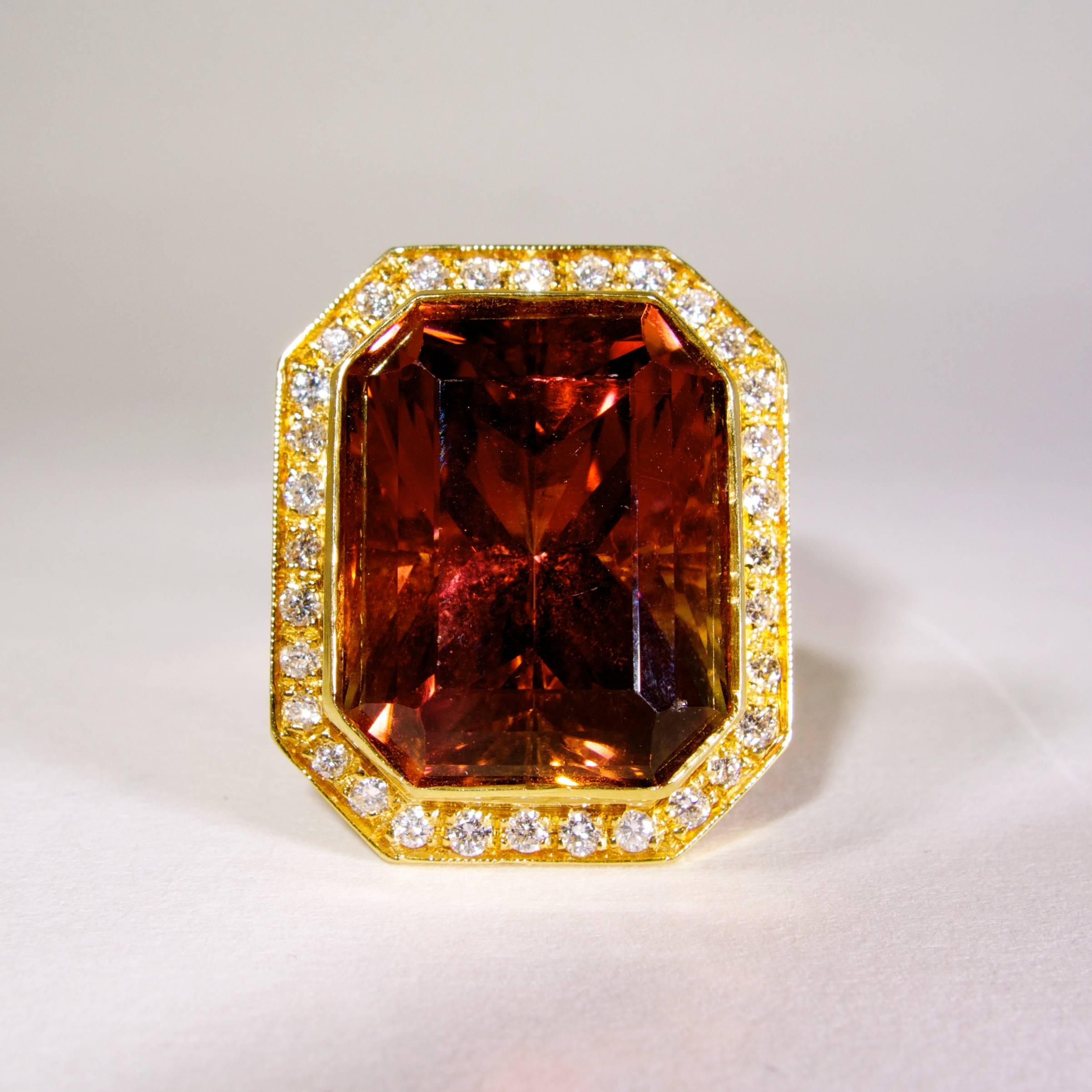 The center tourmaline displays a very unusual color of pinks and oranges. It is clean and bright. This emerald cut stone weighs approximately 27.5 cts.,   It is surrounded by 32 fine round brilliant cut bead set diamonds which, graded in the