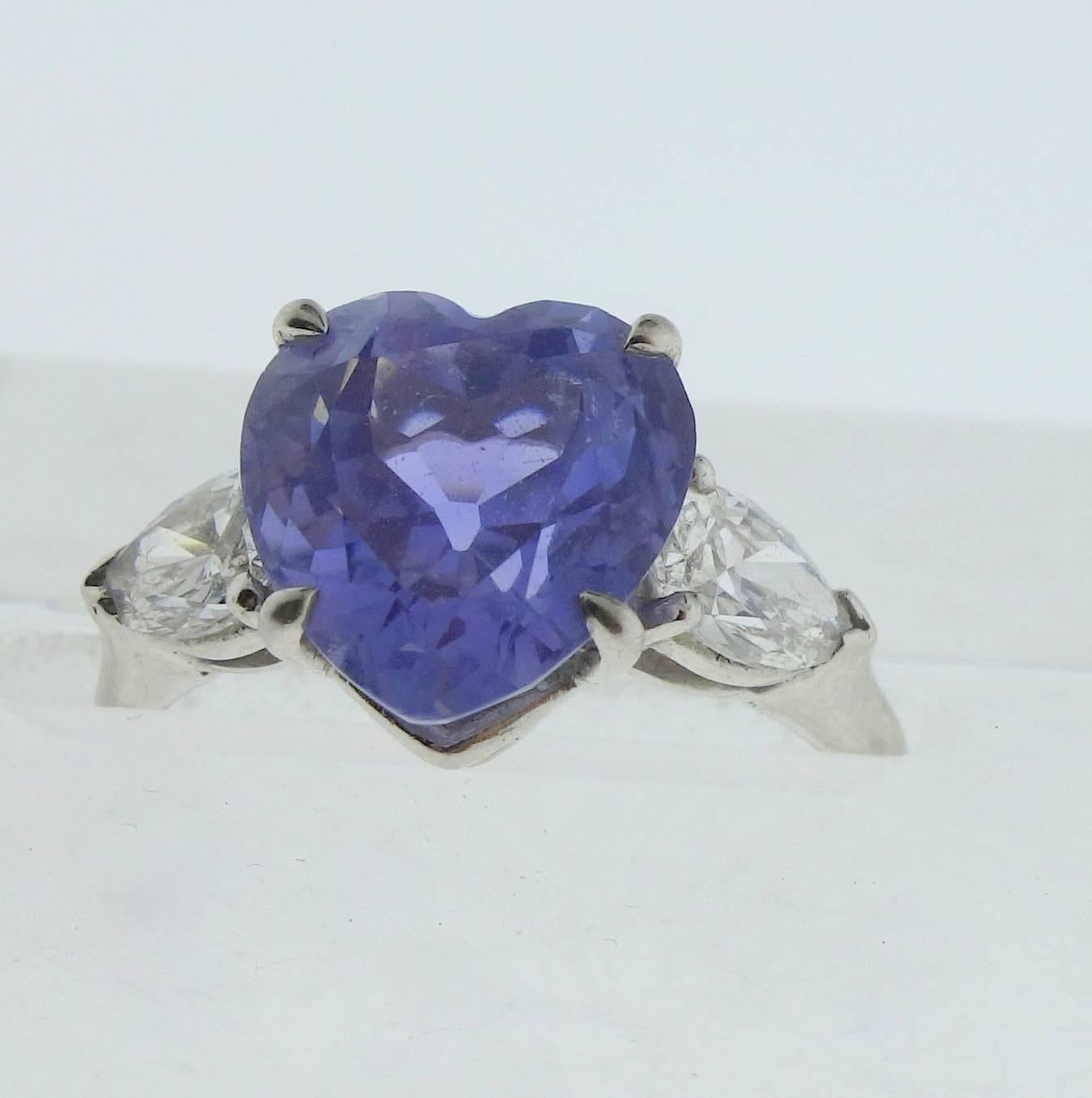 Der zentrale gut geschliffene herzförmige Saphir ist hellblau mit einem leichten violetten Unterton. Er wiegt etwa 4::0 ct. Es hat eine sehr schöne pastellblaue Farbe.  Dieser Mittelstein wird auf beiden Seiten von je 0::33 ct. (ungefähr) feinen
