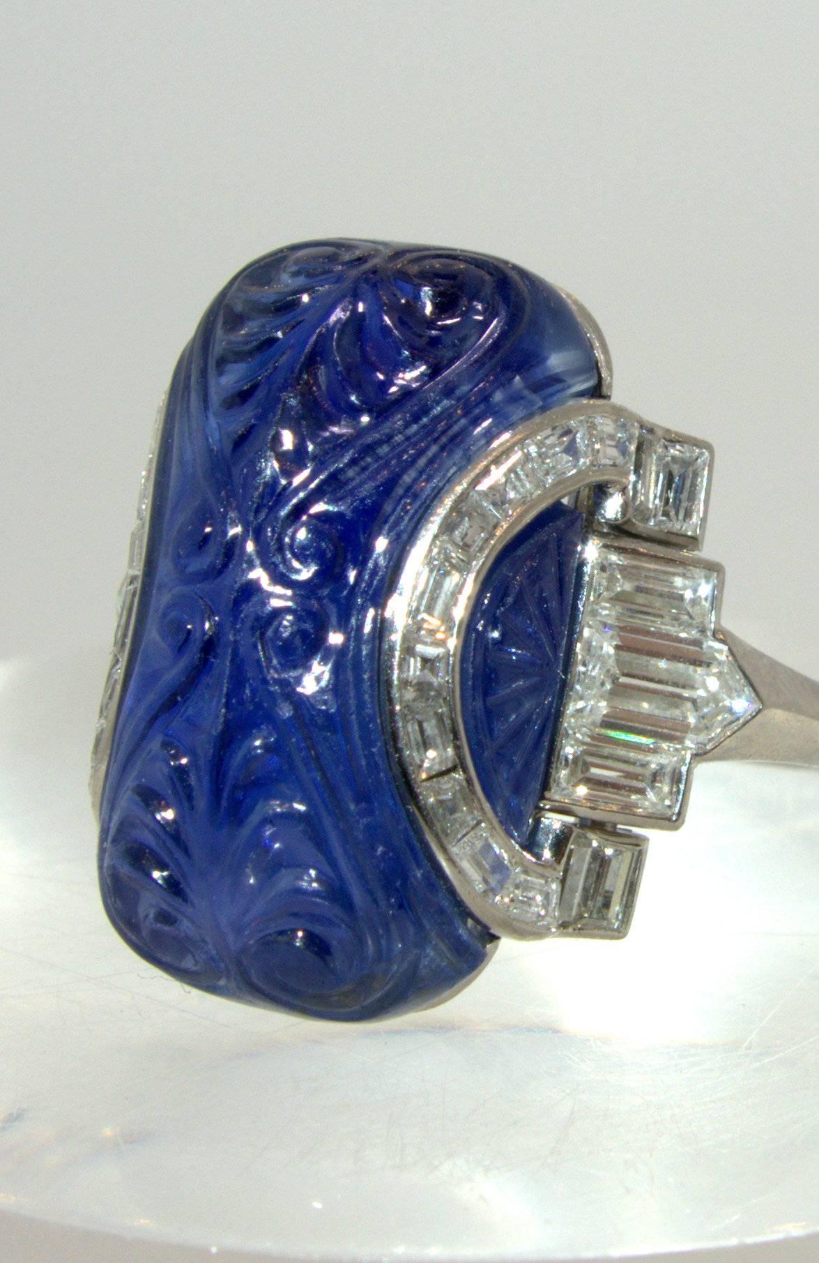 Unusual and striking in design, this Art Deco ring is platinum and possesses an approximated 22 cts., fine hand carved unheated Burma sapphire (accompanied by an AGL certificate) is a bright medium blue color.  It is accented with baguette cut