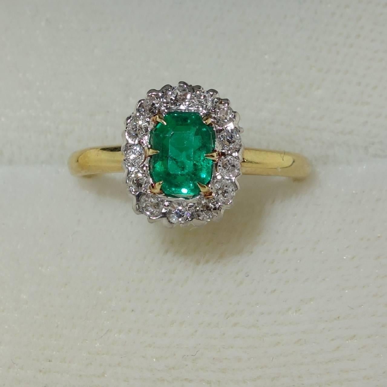 A bright green Colombian emerald is surrounded by 13 old cut diamonds -  all near colorless and very slightly included.  The total diamond weight is approximately .33 cts.  The emerald-cut emerald displays an even clear, medium green color and