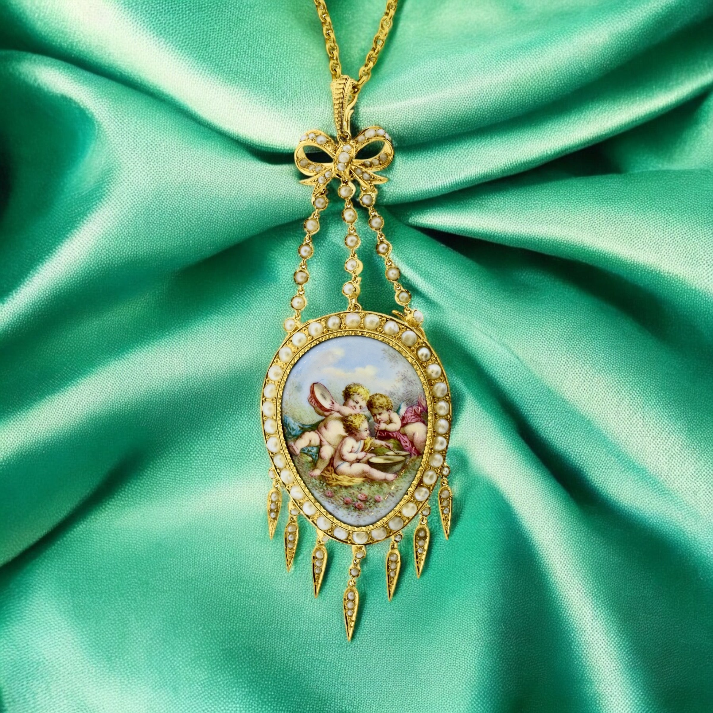 Exquisite substantial pendant necklace crafted in 18k yellow gold. The piece features a detailed enamel painting of cherubs,  surrounded by a border of natural white pearls. The pendant is adorned with a delicate bow motif at the top, from which
