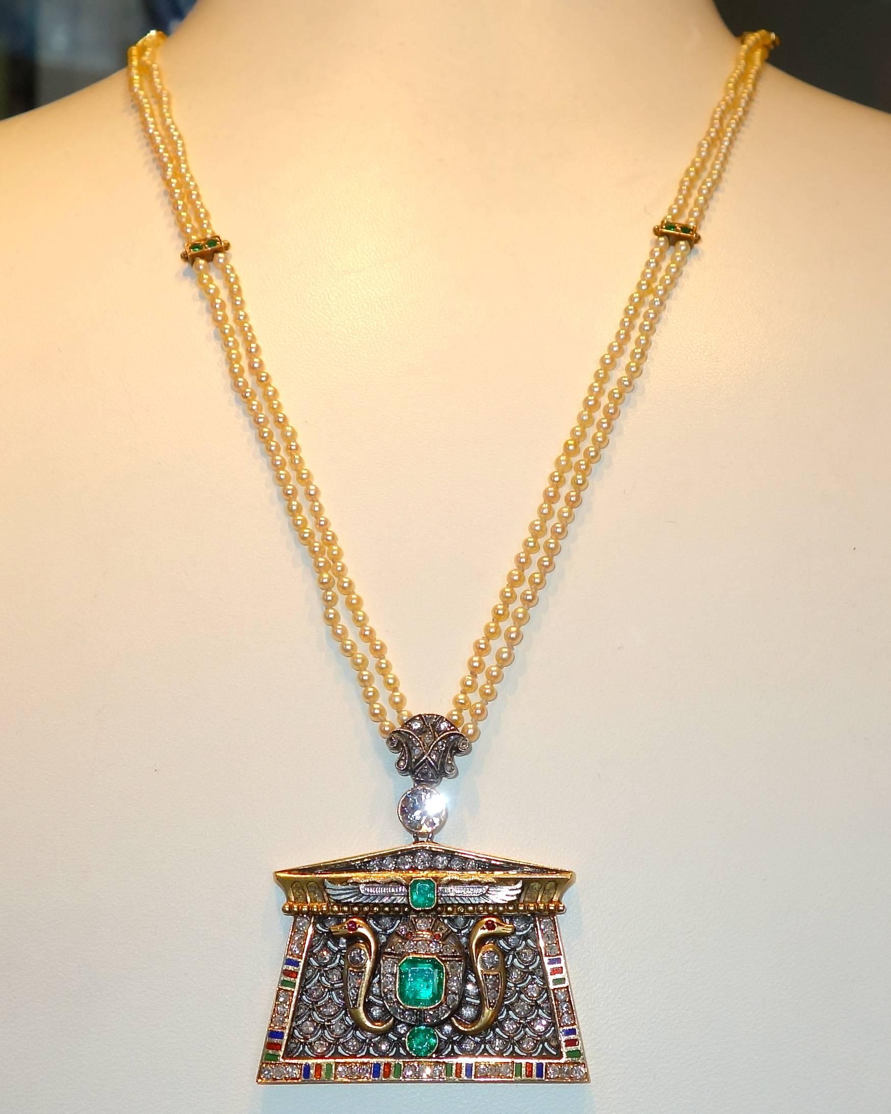 Egyptian revival pendant suspended from natural pearls, this pendant centers natural emeralds (approximately 1 ct.) and older cut diamonds (approximately 1 ct.) and further decorated with multi color enamel.  The opposing serpent's have small ruby