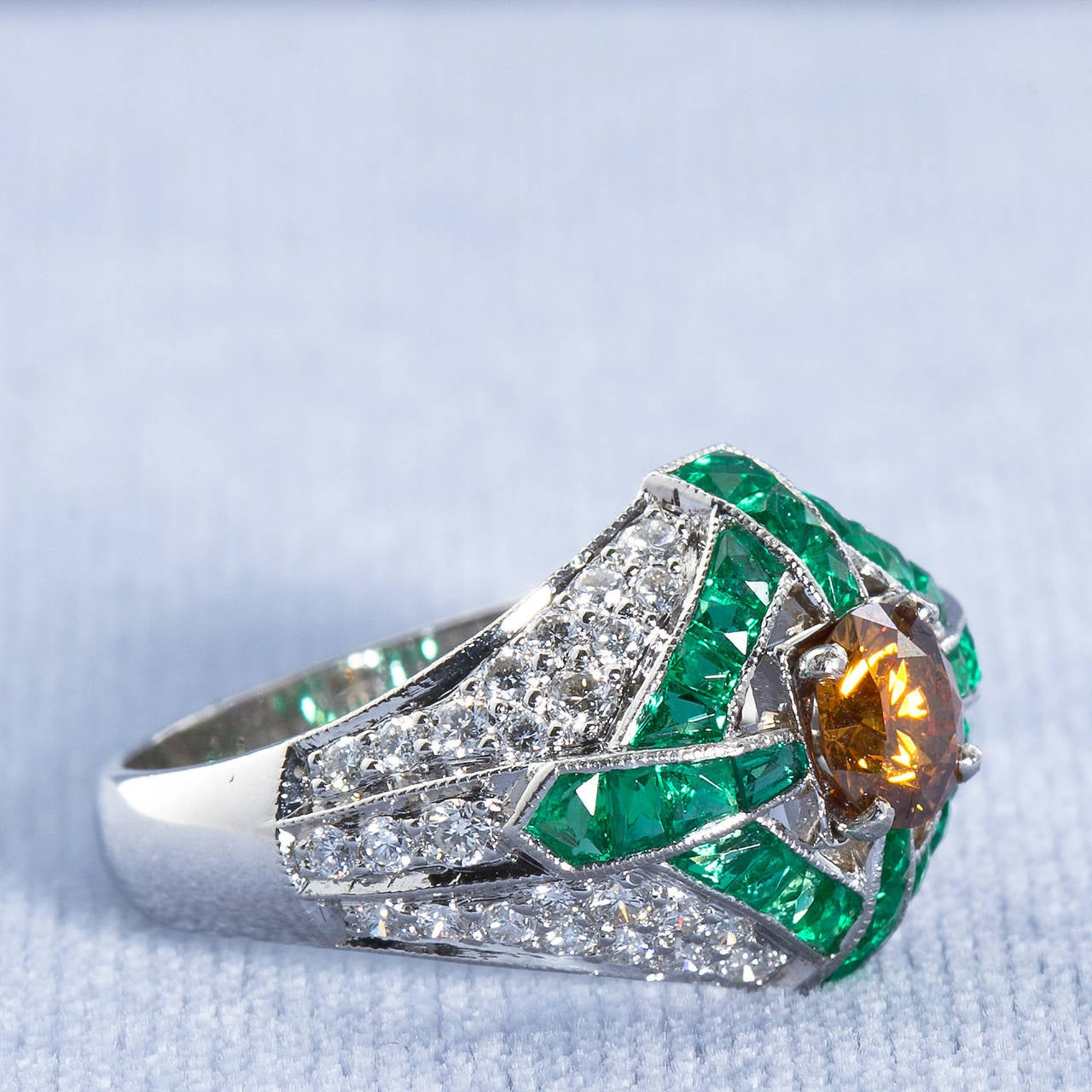 A natural fancy color diamond of vivid orange yellow color set in an elaborate diamond pave domed Art Deco style platinum and calibrated French cut emeralds ring. Center diamond is a round brilliant cut 0.82 carat weight measuring 5.67 - 5.72 x