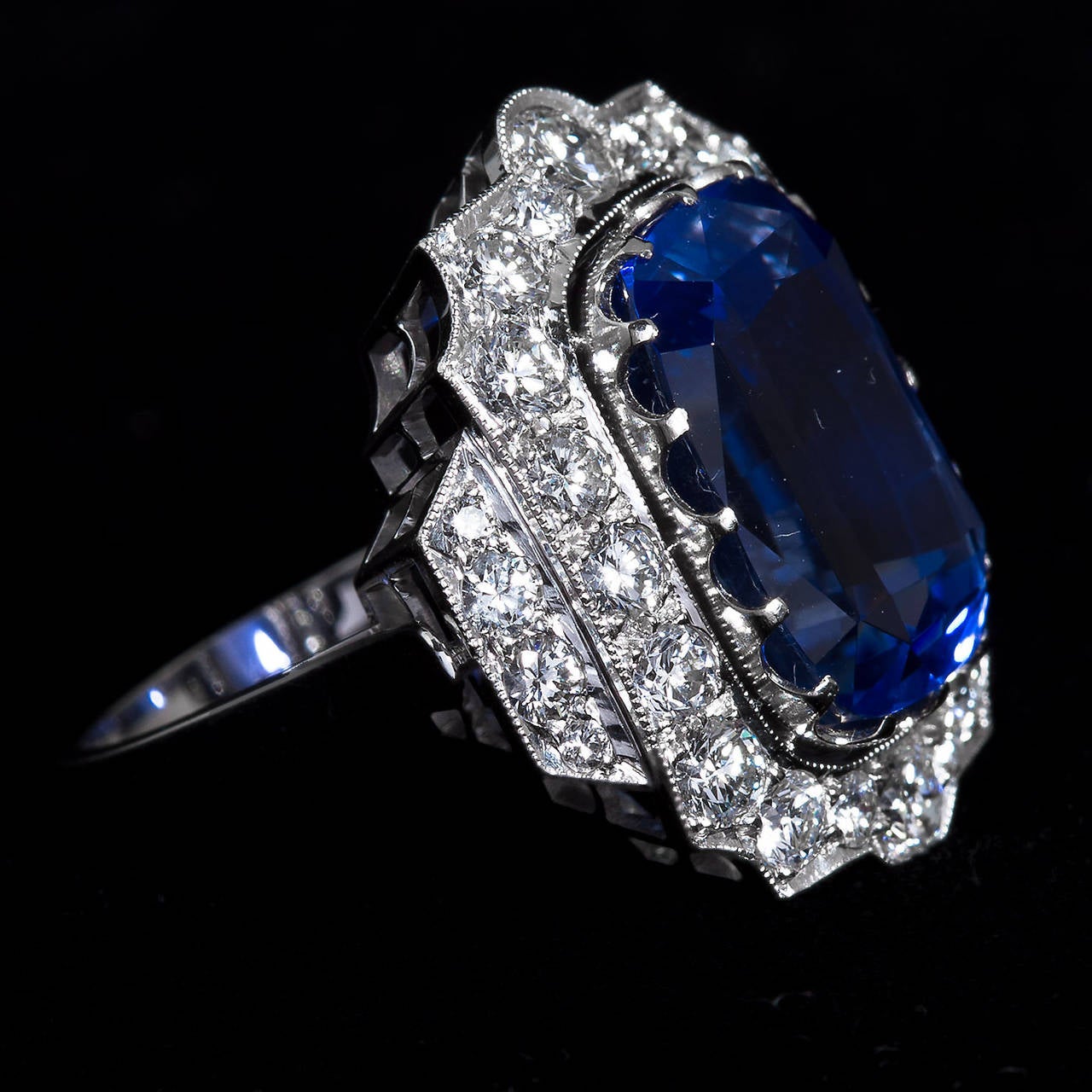 An Art Deco styled ring with a large brilliant blue 16.26 carat cushion cut Ceylon sapphire center stone set in diamond and 18k white gold gallery in a graceful arched styling. Sapphire is not heat treated and measures 15.40 x 11.50 mm. Diamonds are