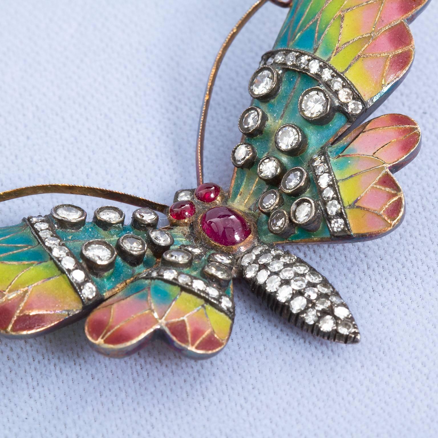 A remarkable Plique-à-jour method enamel butterfly brooch with graduating color enamel in gold wings.  Set with an approx. 0.50 ct oval cabochon ruby and 0.15 ctw round ruby eyes.  Further set with approx. 2.56 ctw antique cut round diamonds. 